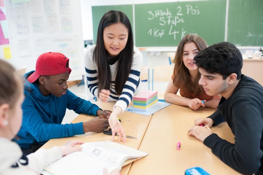 Das Foto zeigt eine junge Frau, die vier Schüler:innen in einem Klassenzimmer Nachhilfeunterricht gibt.