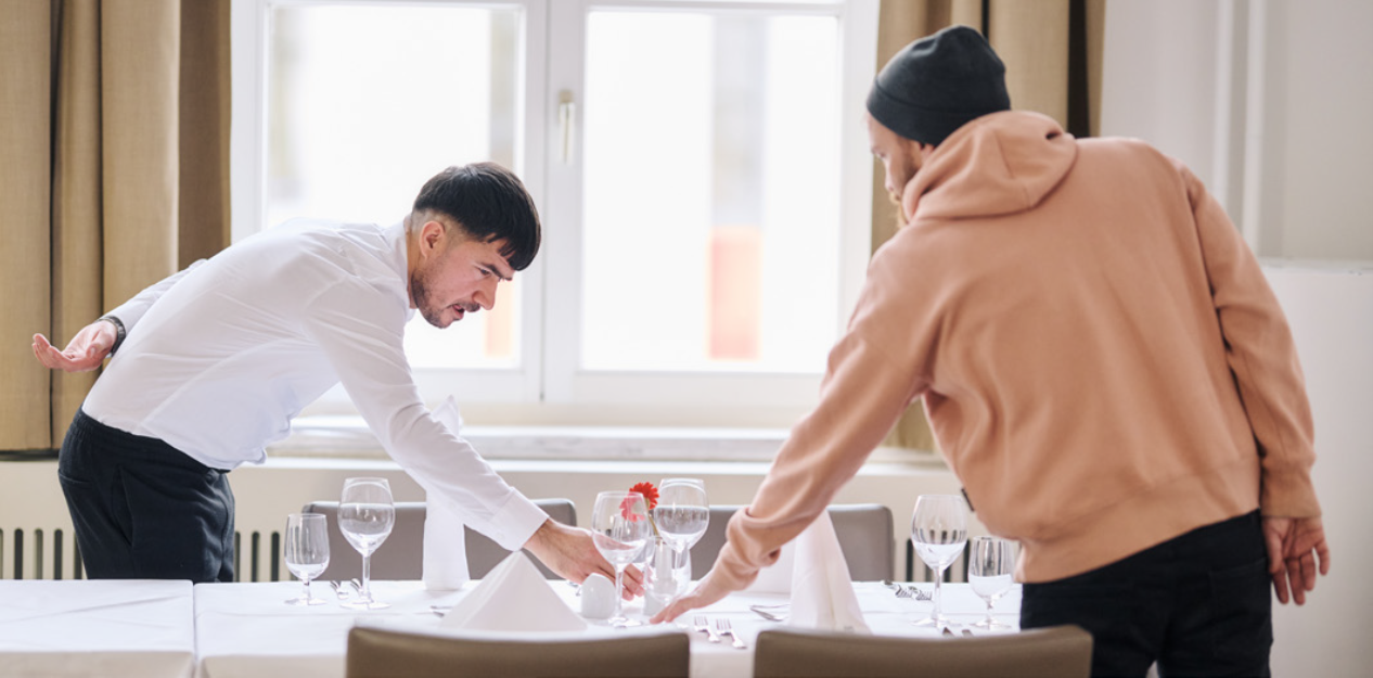 Auf dem Foto sind zwei Männer erkennbar, die einen Tisch mit Gläsern eindecken. Auf dem Foto sind zwei Männer erkennbar, die einen Tisch mit Gläsern eindecken.
