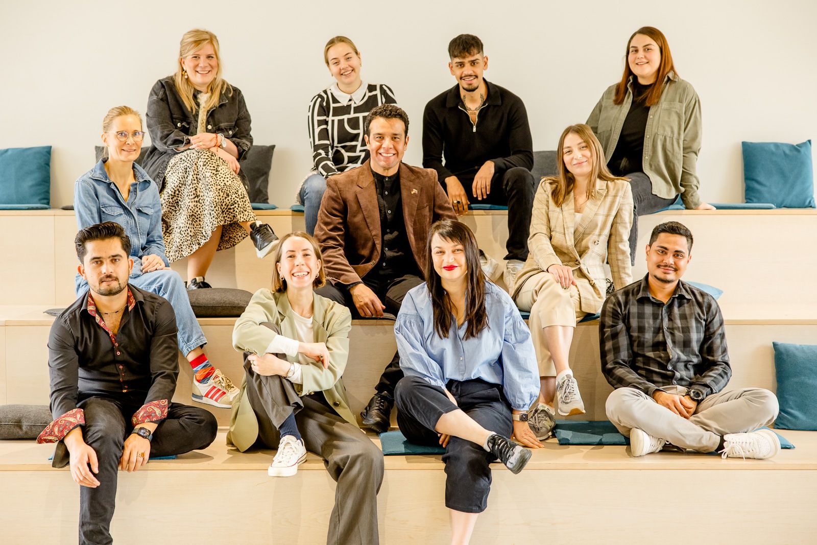 Das Foto zeigt eine Gruppe von Menschen unterschiedlichen Alters, die auf einer Treppe sitzen und in die Kamera gucken.