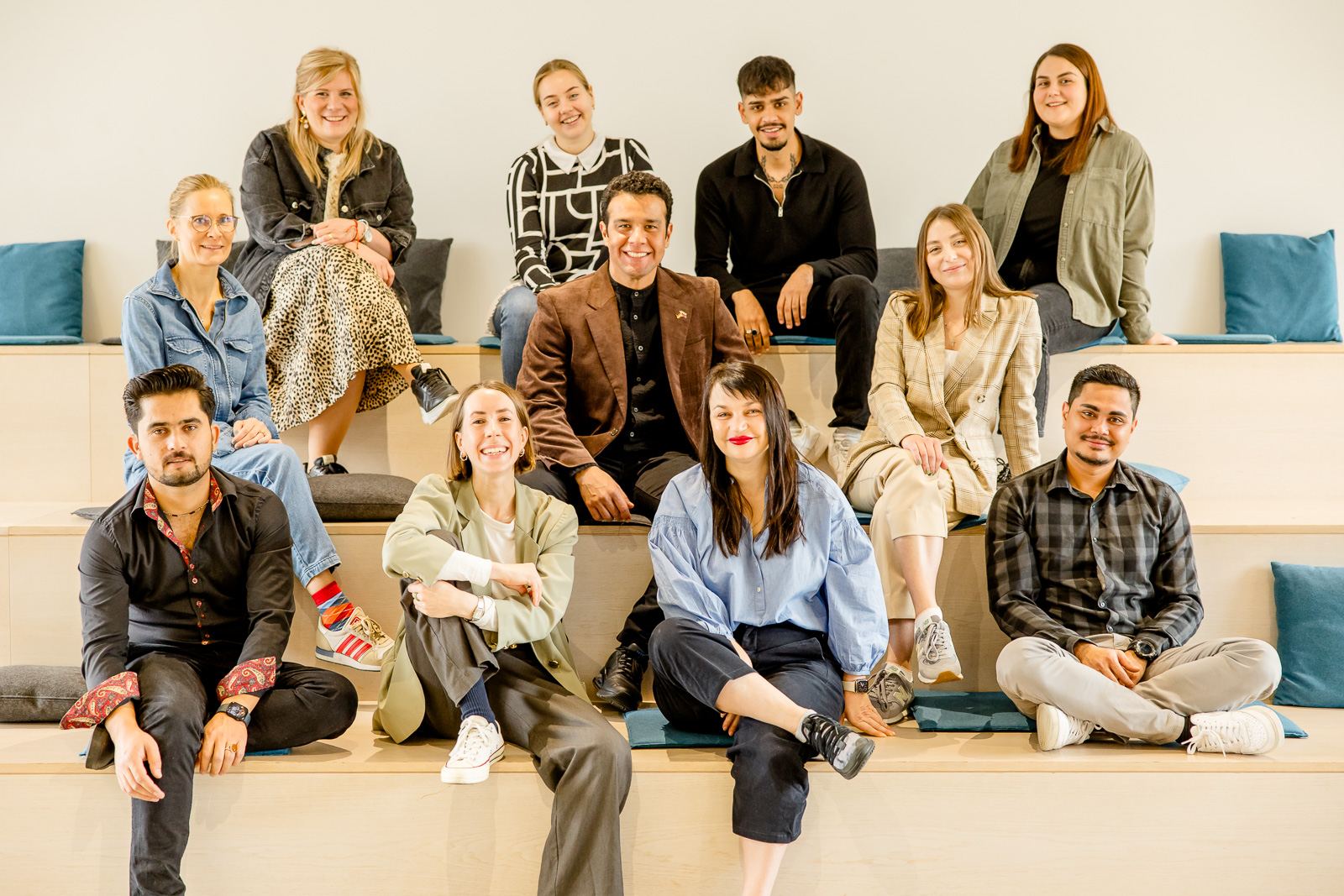 Das Foto zeigt eine Gruppe von Menschen unterschiedlichen Alters, die auf einer Treppe sitzen und in die Kamera gucken. Das Foto zeigt eine Gruppe von Menschen unterschiedlichen Alters, die auf einer Treppe sitzen und in die Kamera gucken.