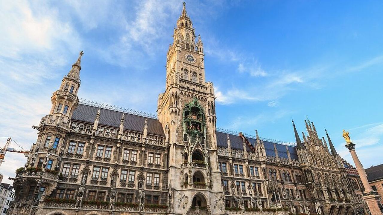 Neues Rathaus in München mit historischer Fassade und Turmuhr bei strahlend blauem Himmel, umgeben von Menschen auf dem Marienplatz. Neues Rathaus in München mit historischer Fassade und Turmuhr bei strahlend blauem Himmel, umgeben von Menschen auf dem Marienplatz.