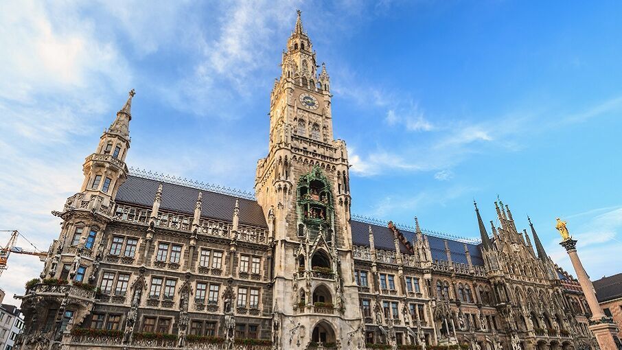 Neues Rathaus in München mit historischer Fassade und Turmuhr bei strahlend blauem Himmel, umgeben von Menschen auf dem Marienplatz.