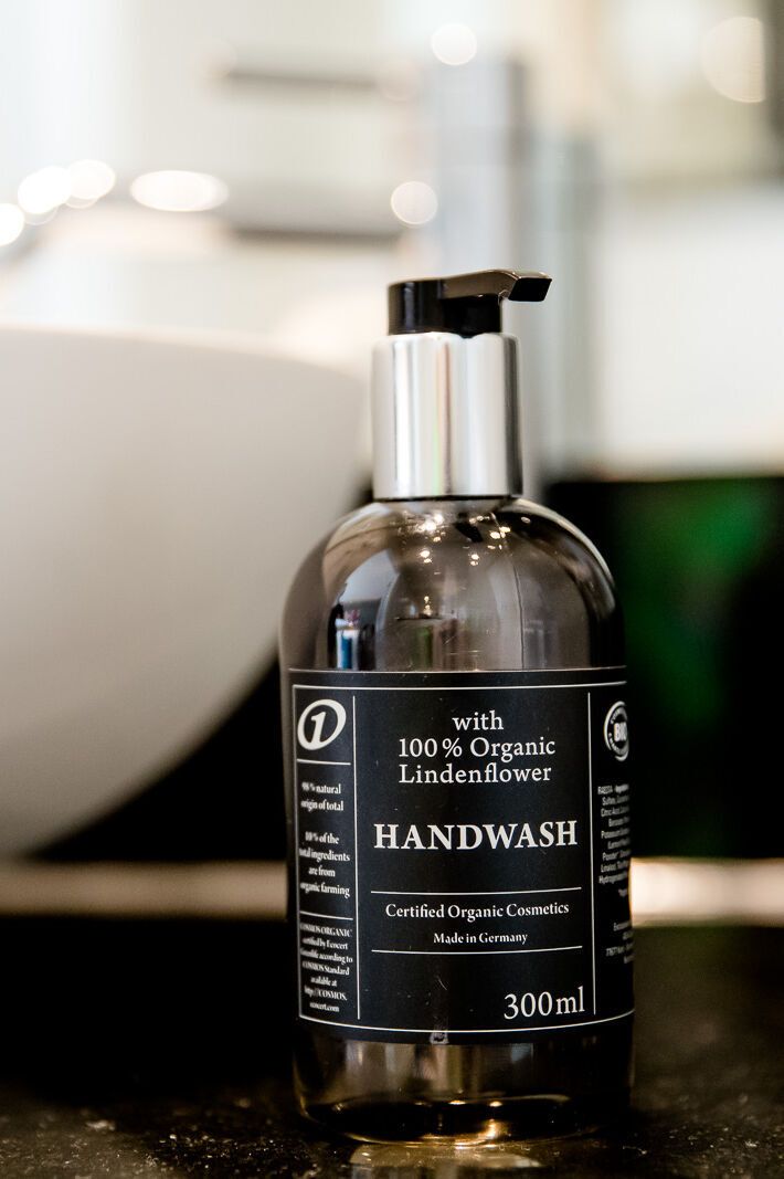Flasche mit flüssiger Handseife aus 100 % biologischer Lindenblüte neben weißem Waschbecken auf schwarzer Oberfläche, modernes Badezimmerambiente.