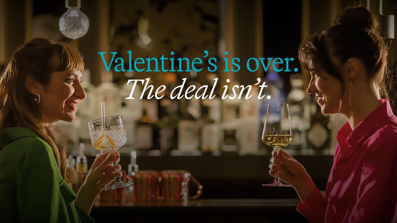 Zwei Frauen stoßen in einer stilvollen Bar mit Getränken an und lächeln sich an, vermittelt eine gemütliche, freundschaftliche Atmosphäre jenseits von Valentinstag-Angeboten.