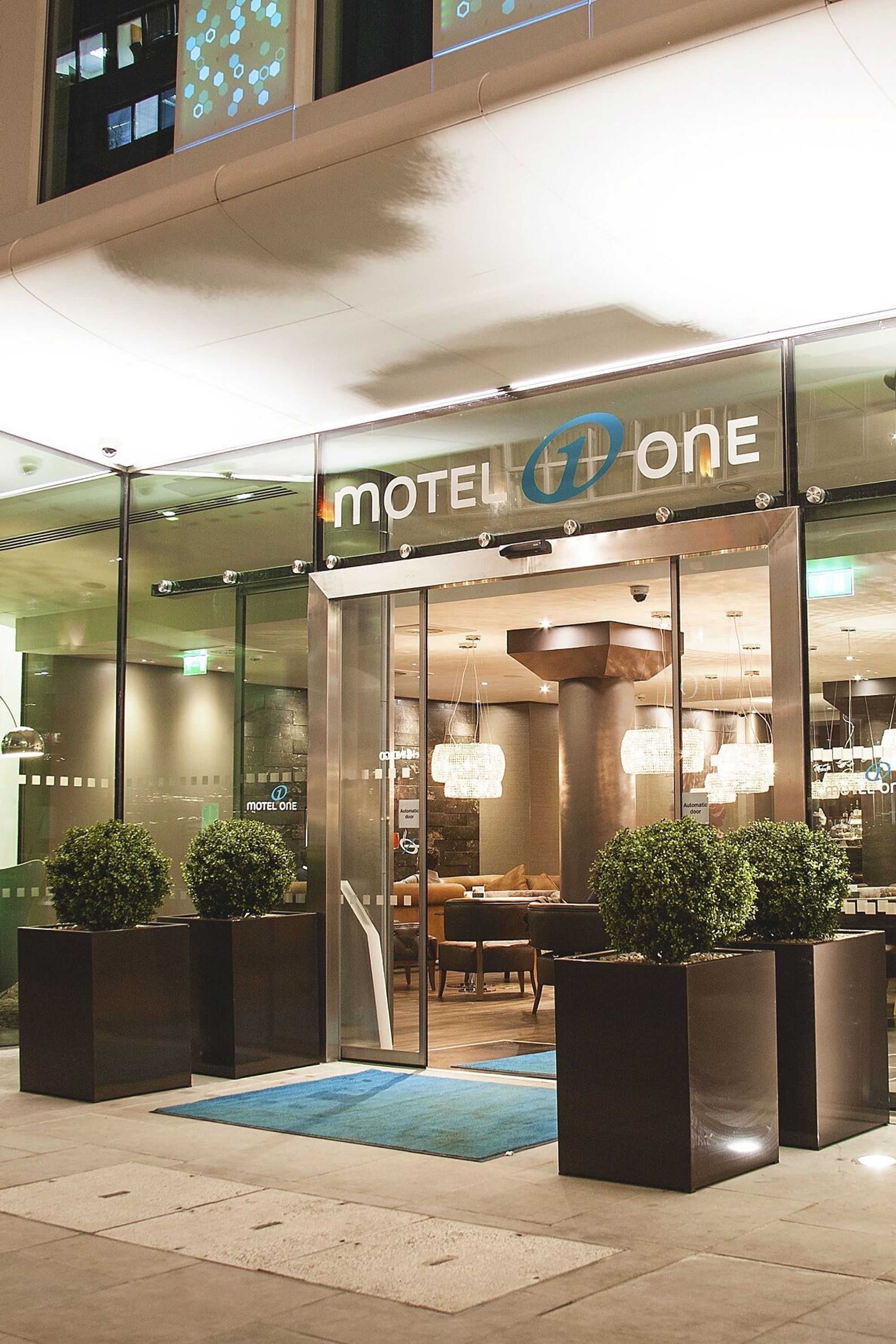 hotel London Tower Hill Motel One view from outside of the brightly lit entrance area at night