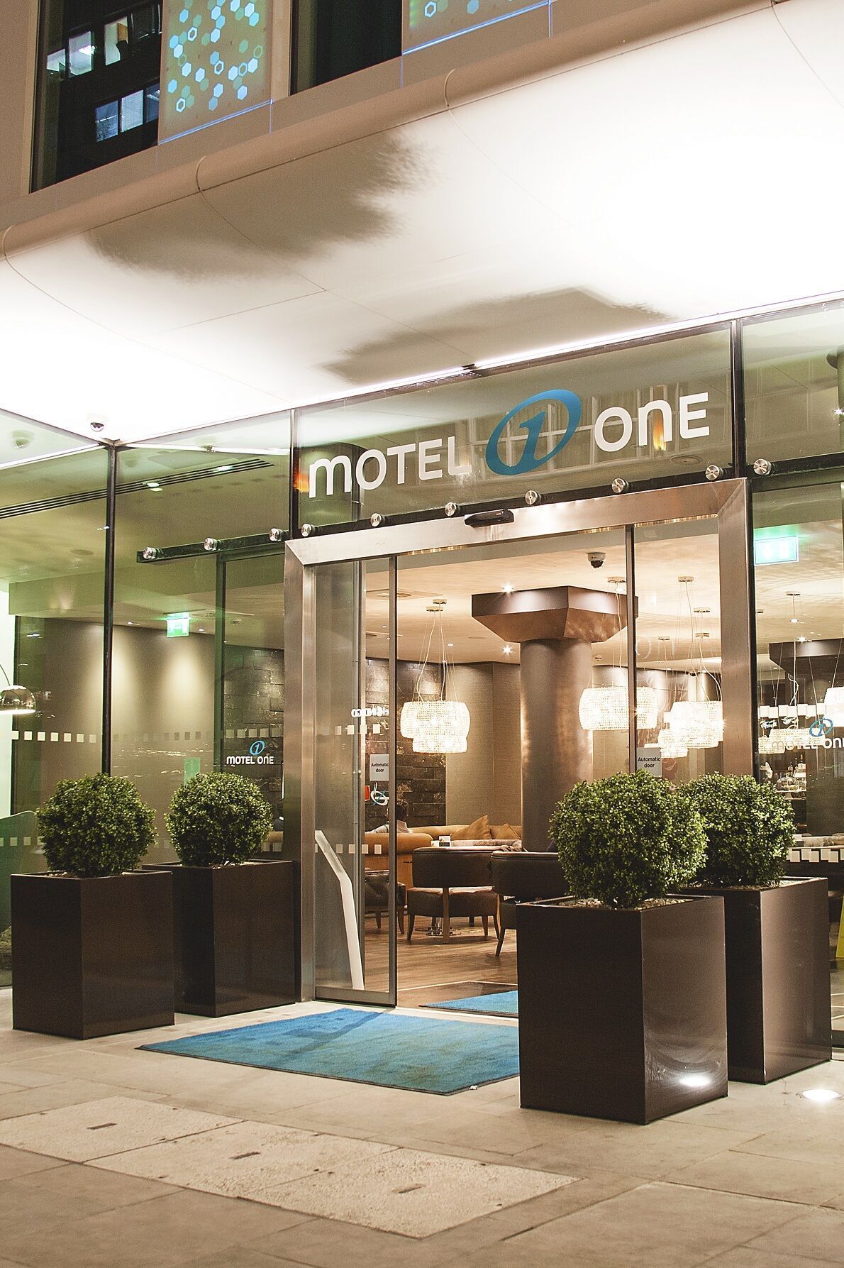 hotel London Tower Hill Motel One view from outside of the brightly lit entrance area at night