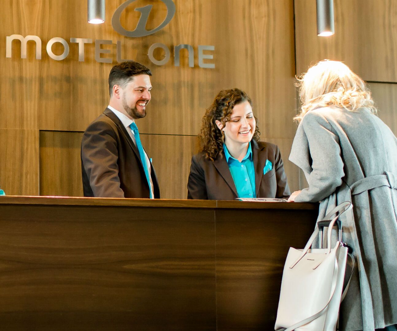 Rezeptionsteam begrüßt eine Gästin an der Empfangstheke eines modernen Hotels mit freundlichem Service und professioneller Atmosphäre.