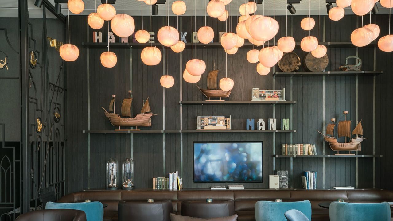 Gemütliche Lobby mit dunkelblauen Sesseln, runden Tischen und weicher Beleuchtung durch viele hängende Lampen, ergänzt durch maritime Deko und Bücherregale für entspannte Aufenthalte. Gemütliche Lobby mit dunkelblauen Sesseln, runden Tischen und weicher Beleuchtung durch viele hängende Lampen, ergänzt durch maritime Deko und Bücherregale für entspannte Aufenthalte.