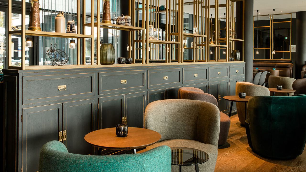 Hotel München Parkstadt Schwabing Motel One Lounge mit Sesseln, Beistelltischen und großem offenen Regal