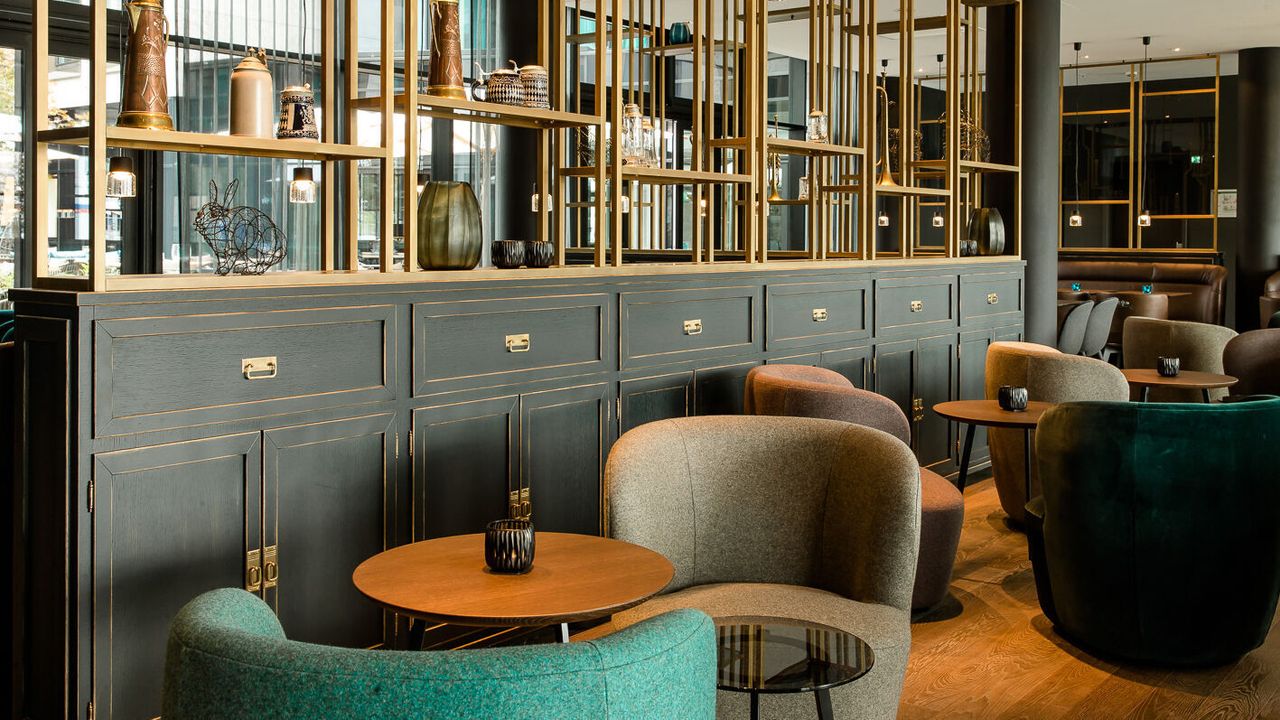 hotel Munich Parkstadt Schwabing Motel One lounge with armchairs, side tables and large open shelving