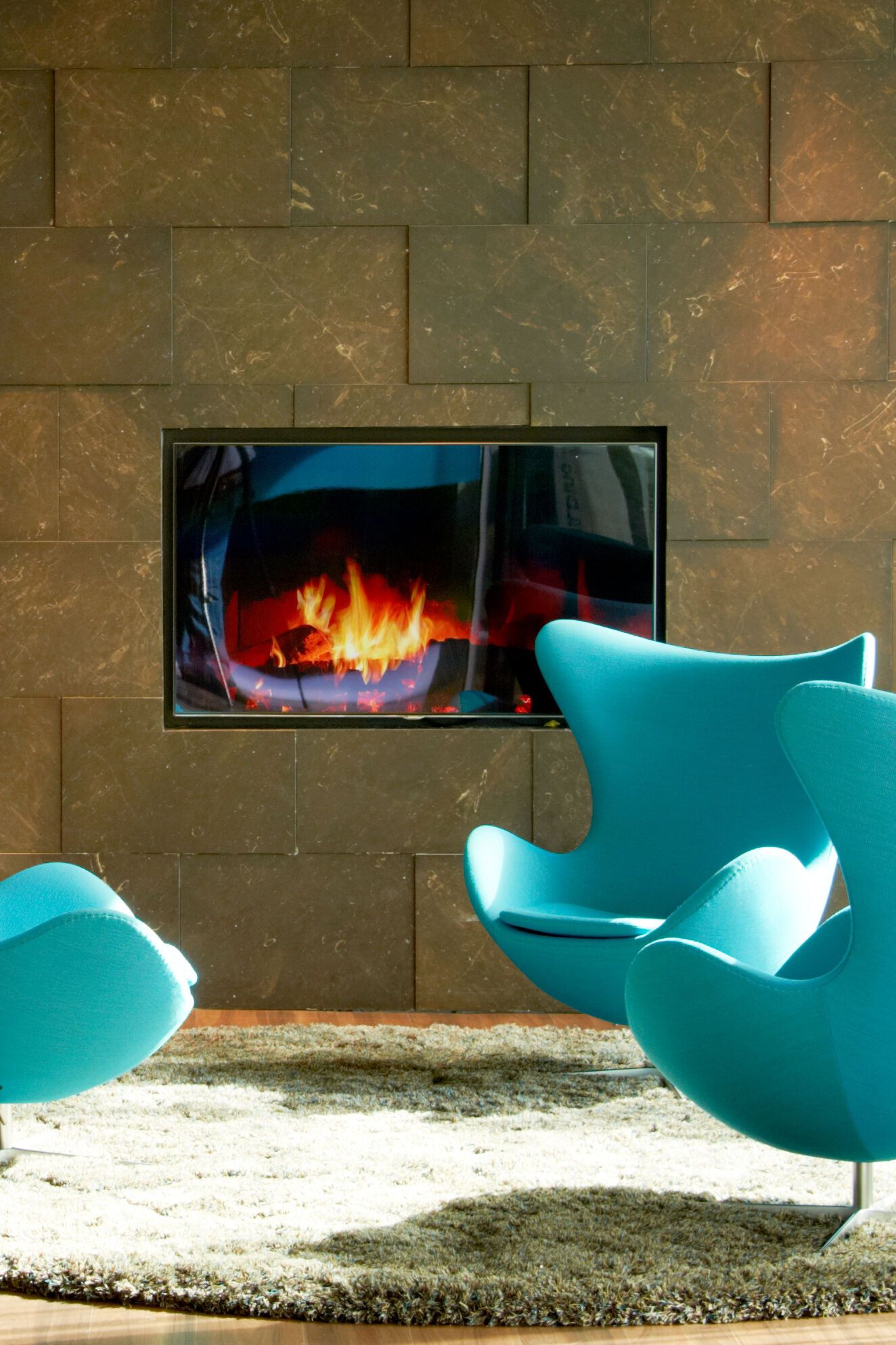 Hotel Amsterdam Motel One drei Egg Chairs vor einem TV mit Kaminbild