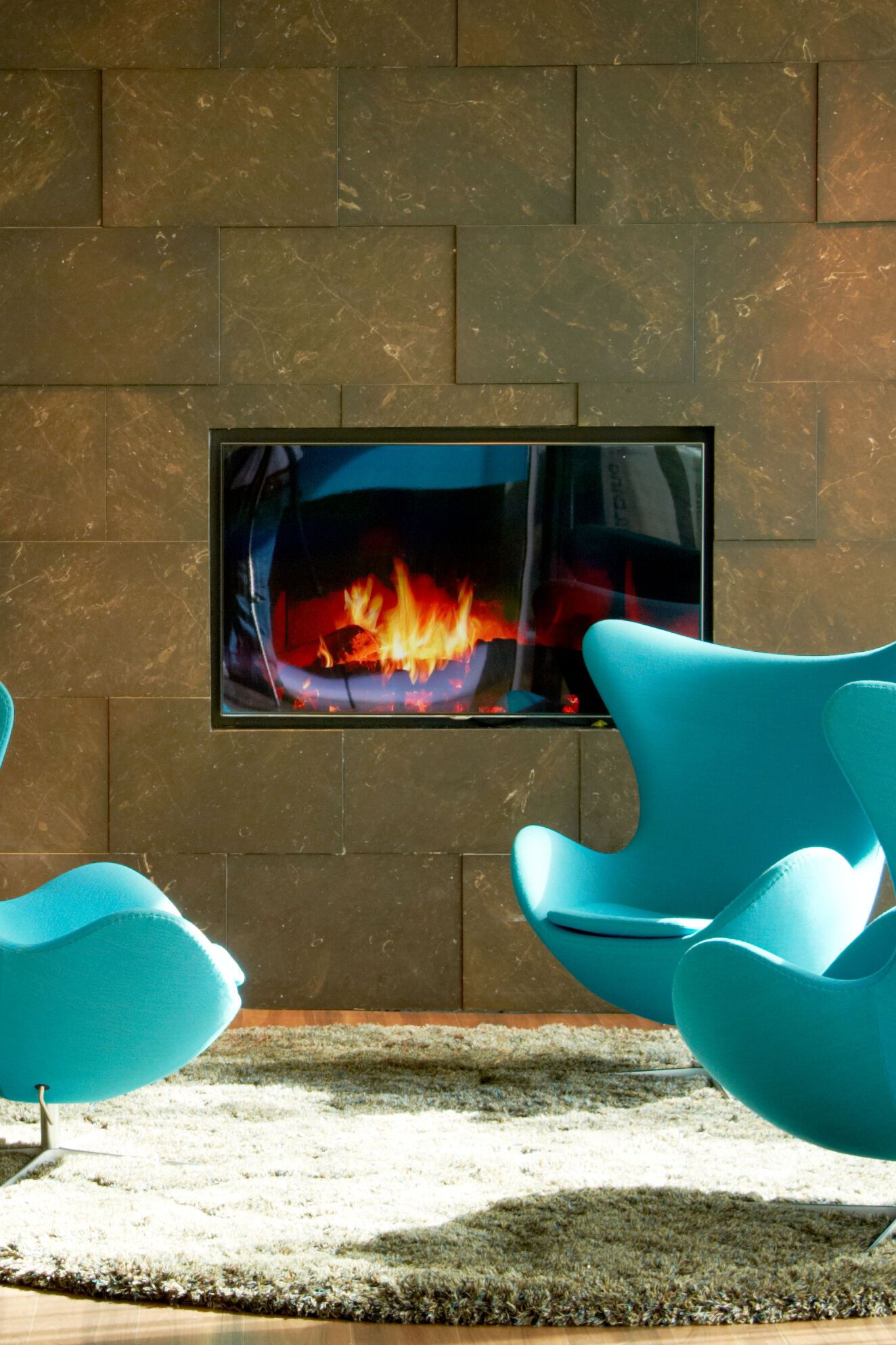 Hotel Amsterdam Motel One drei Egg Chairs vor einem TV mit Kaminbild