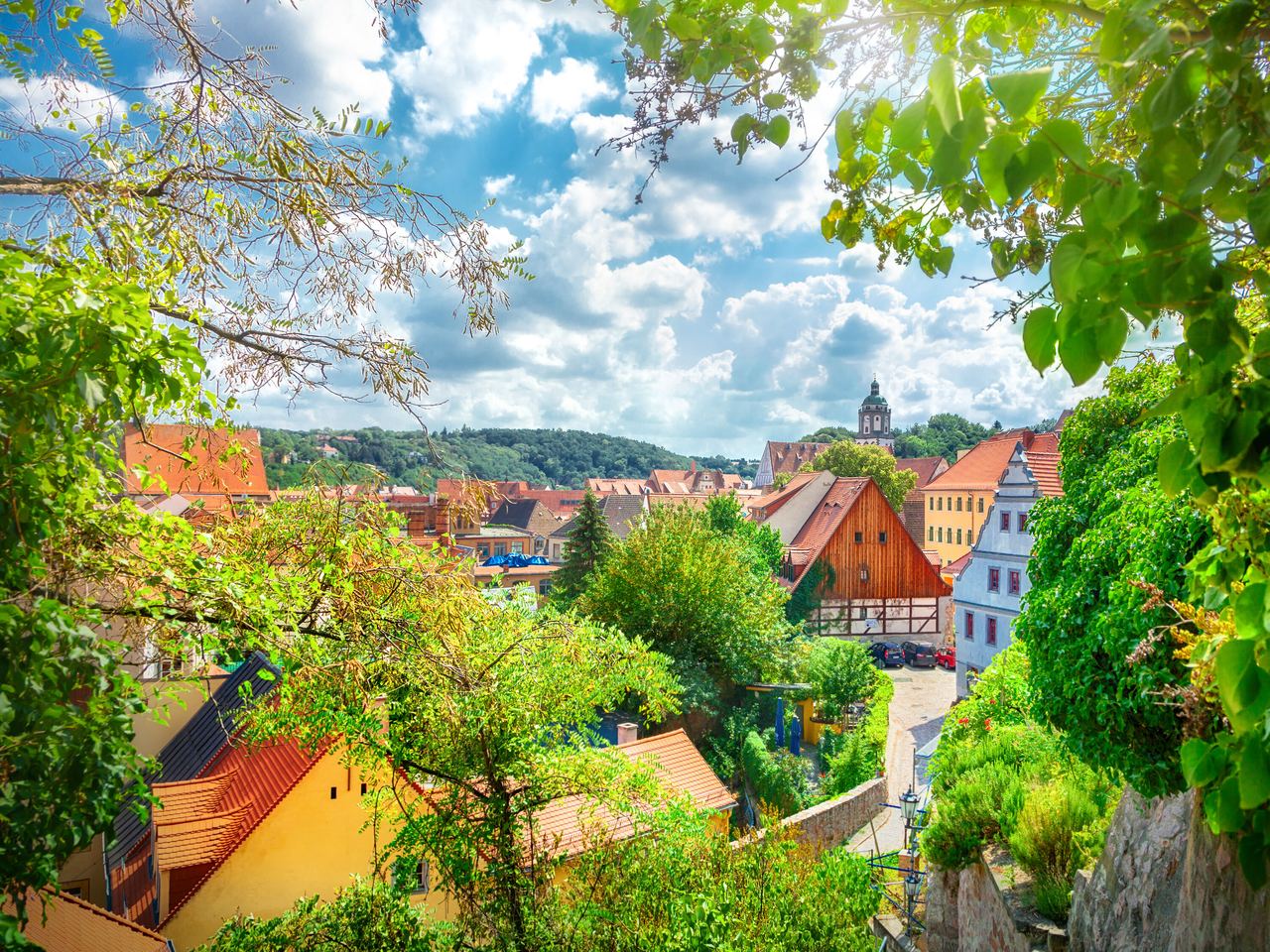 Blick auf eine malerische Kleinstadt mit historischen Fachwerkhäusern, grünen Bäumen und einem bewölkten Himmel, ideal für ruhige Spaziergänge und kulturelle Entdeckungen.