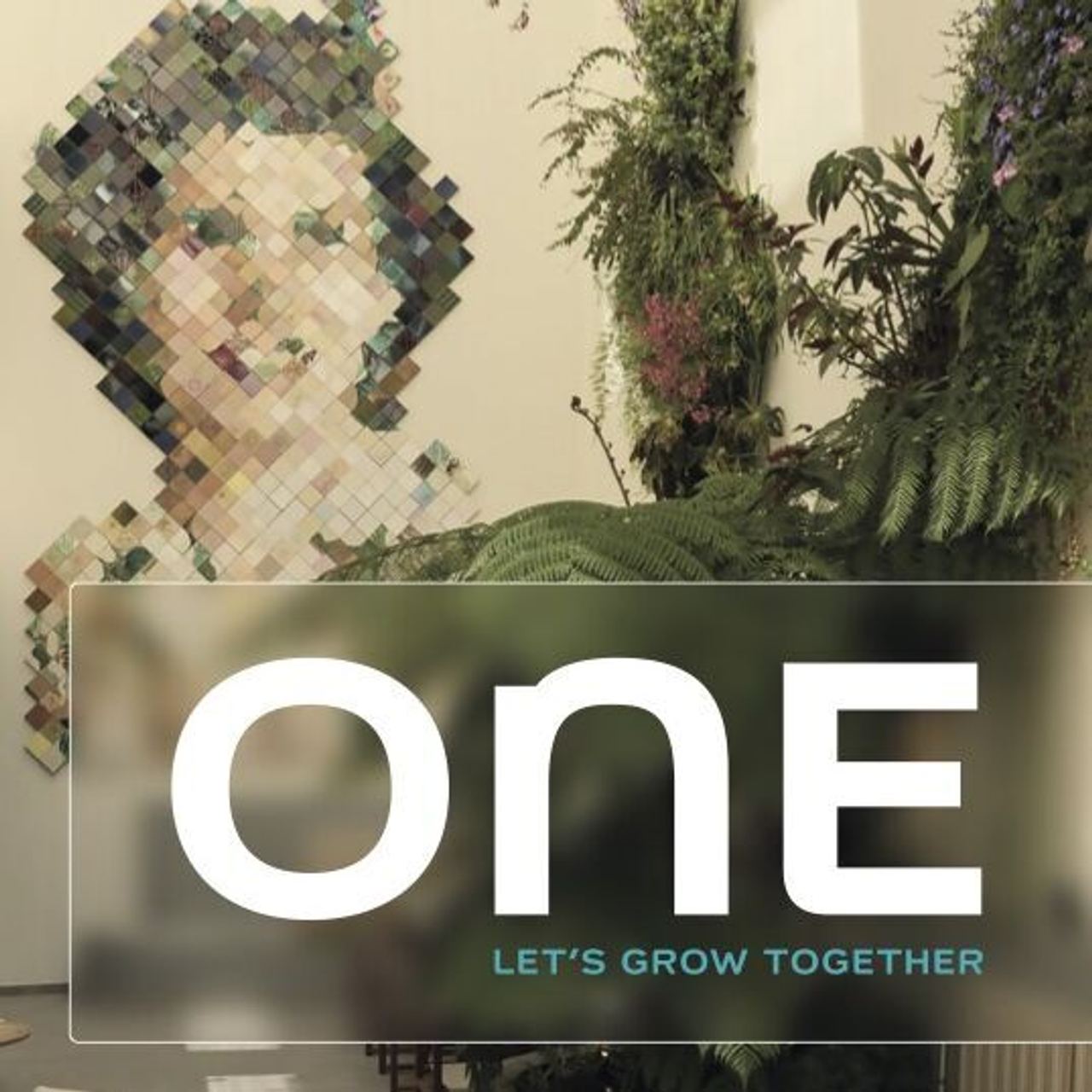 Moderne Lobby mit grünen Pflanzen und stilvoller Sitzgelegenheit. Wandkunst zeigt ein pixeliertes Gesicht, symbolisiert Zusammenhalt. Schriftzug „ONE – Let’s Grow Together“ unterstreicht Gemeinschaft und Wachstum.