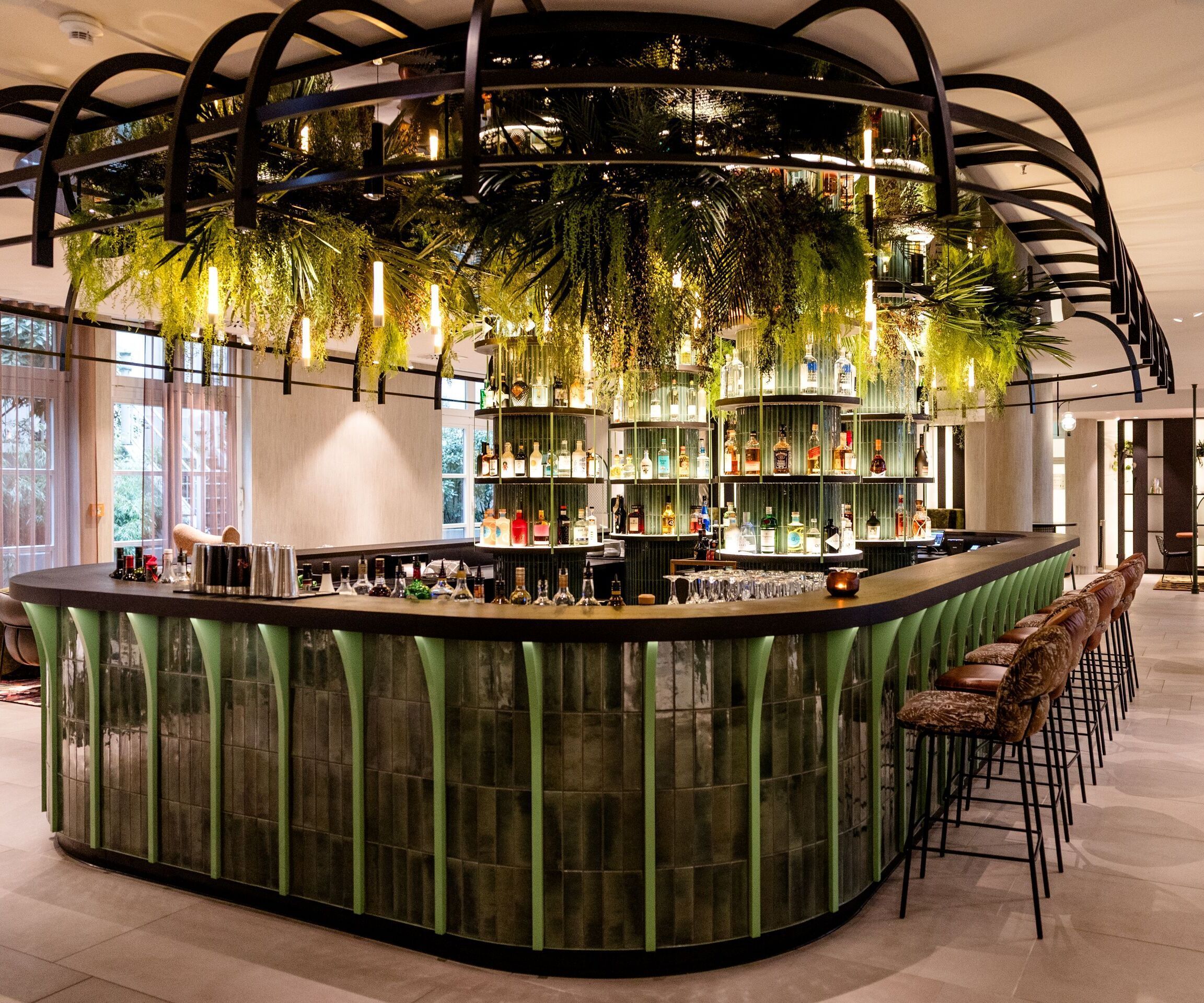 Hotel Frankfurt-Hauptbahnhof Motel One Bar mit grün akzentuierter Theke, hohen Barhockern und hängenden Pflanzen als natürlichem Dekoelement.