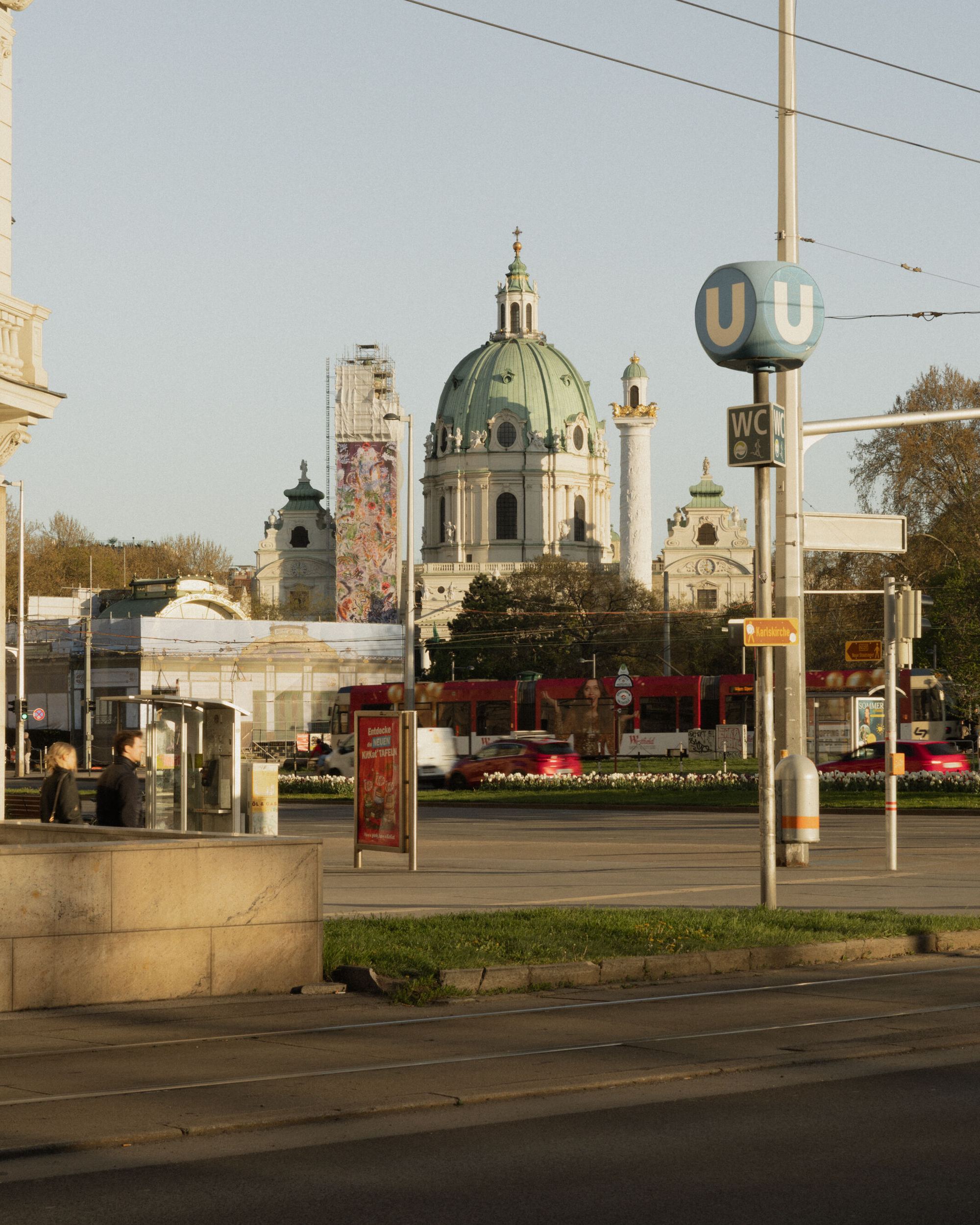Blick auf die historische Karlskirche mit ihrer grünen Kupferkuppel im Herzen Wiens, umgeben von moderner Stadtinfrastruktur und öffentlichem Nahverkehr.