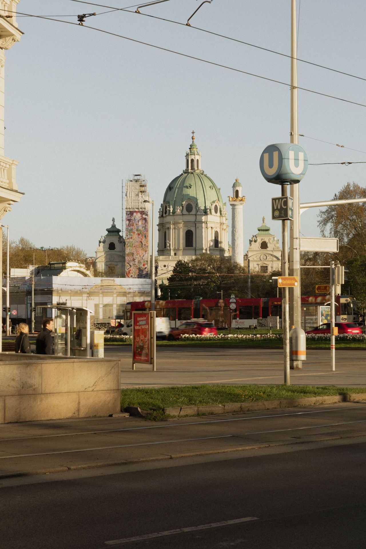 Blick auf die historische Karlskirche mit ihrer grünen Kupferkuppel im Herzen Wiens, umgeben von moderner Stadtinfrastruktur und öffentlichem Nahverkehr.