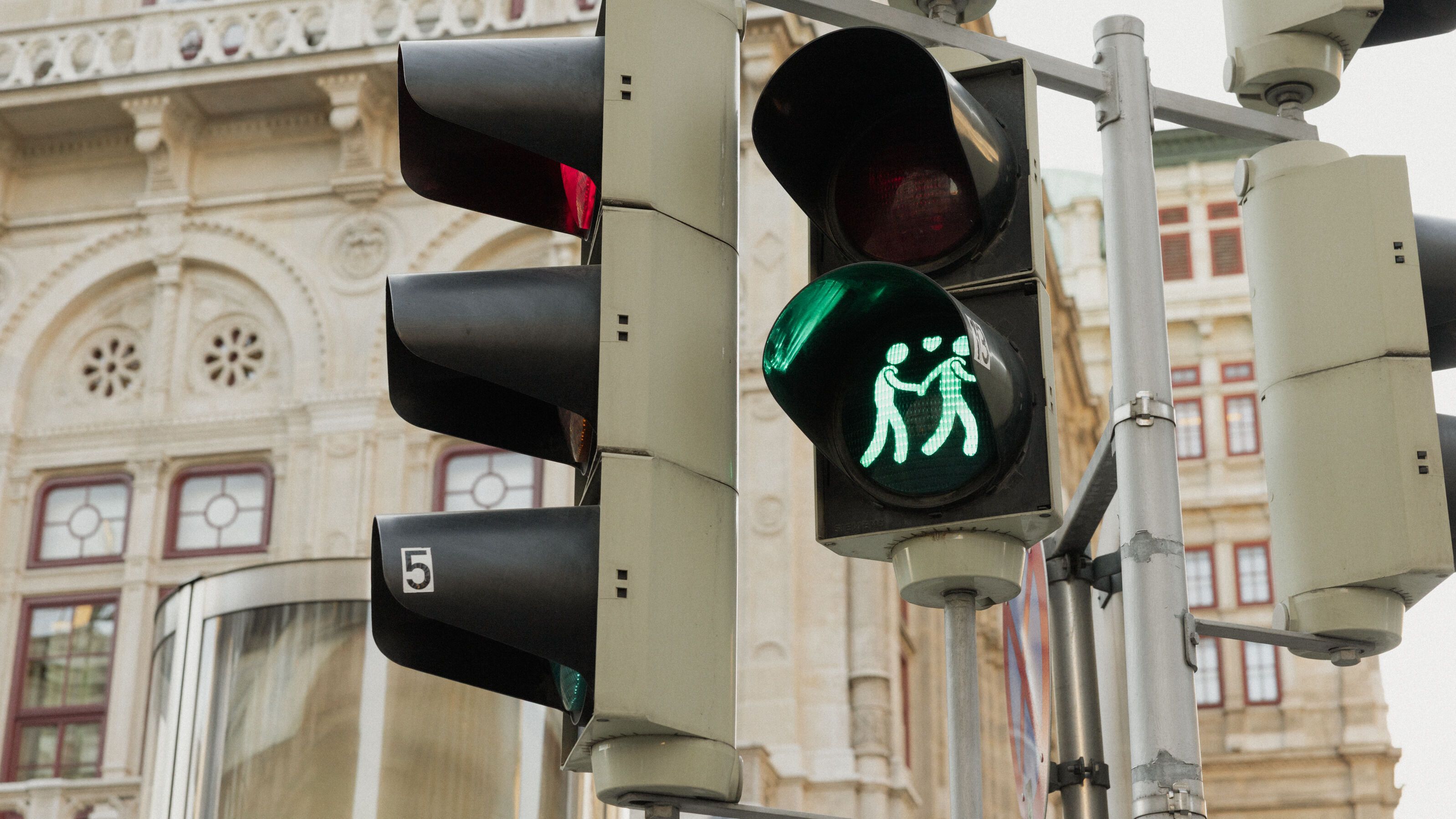 Eine Fußgängerampel mit grünem Lichtsignal, das eine Familie mit zwei Erwachsenen und einem Kind darstellt, symbolisiert sicheres Überqueren der Straße.