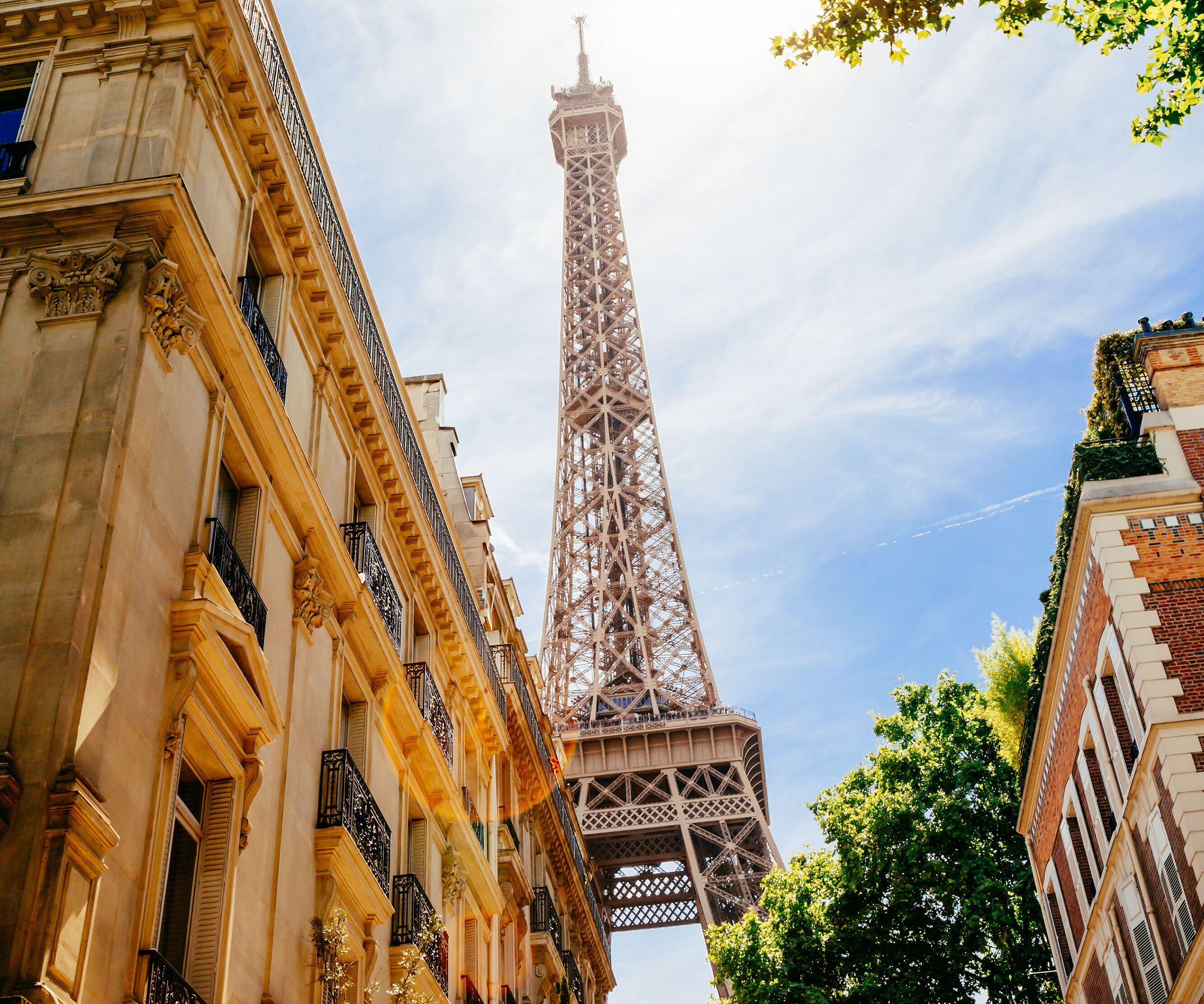 Blick auf den Eiffelturm in Paris bei Sonnenschein, umgeben von historischen Gebäuden und grünen Bäumen, die eine lebendige Stadtkulisse schaffen.