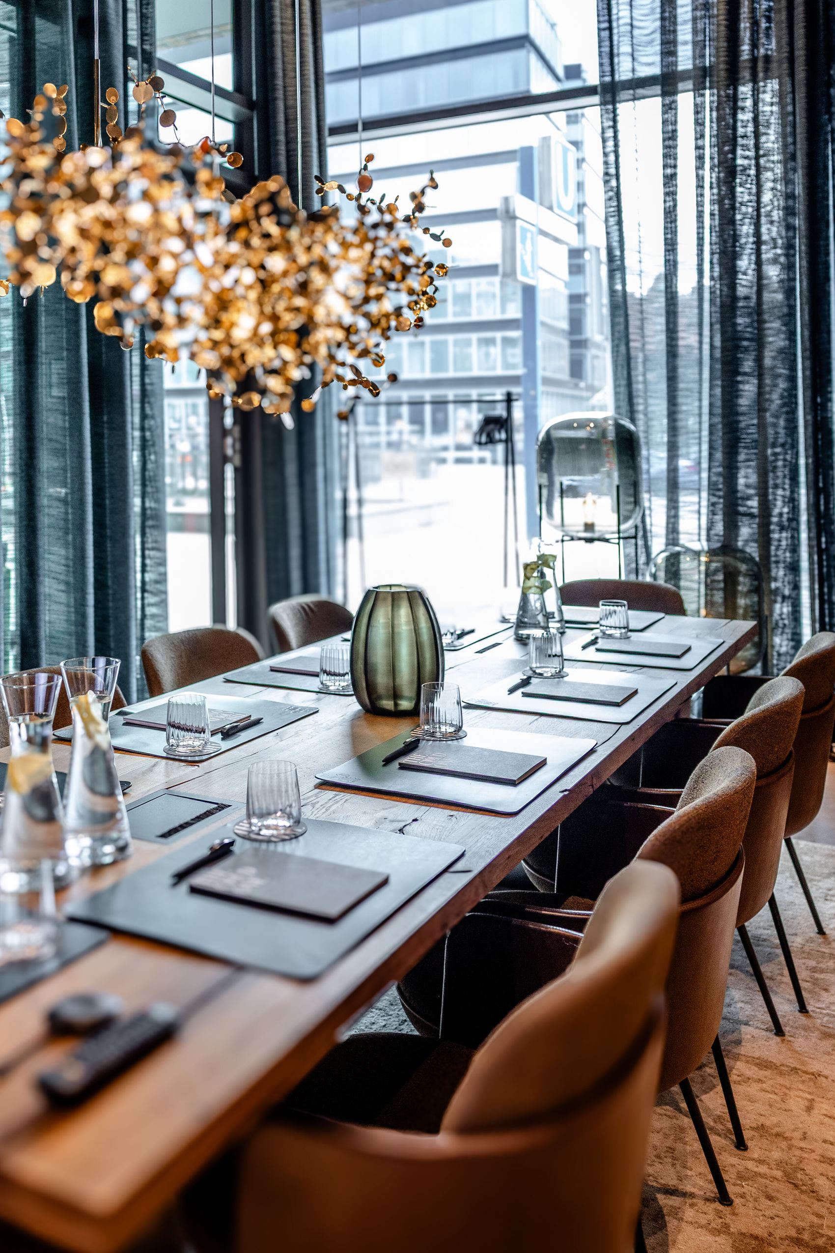 Moderner Konferenzraum mit langem Holztisch, Lederstühlen, eleganter Beleuchtung und großen Fenstern mit Blick auf urbane Architektur, ideal für geschäftliche Besprechungen.