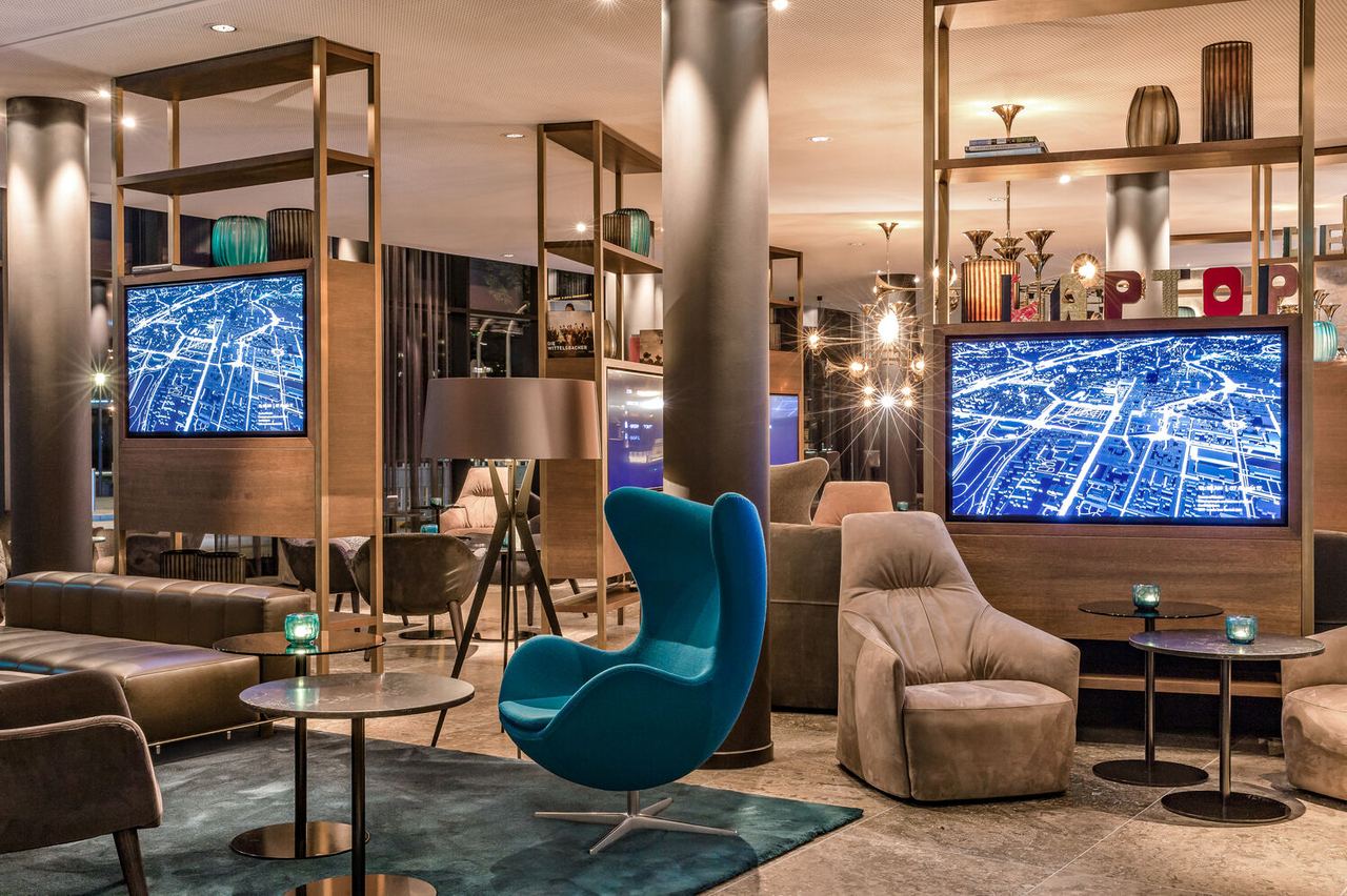 hotel Munich Parkstadt Schwabing Motel One lounge in the evening with two TVs, armchairs and egg chairs