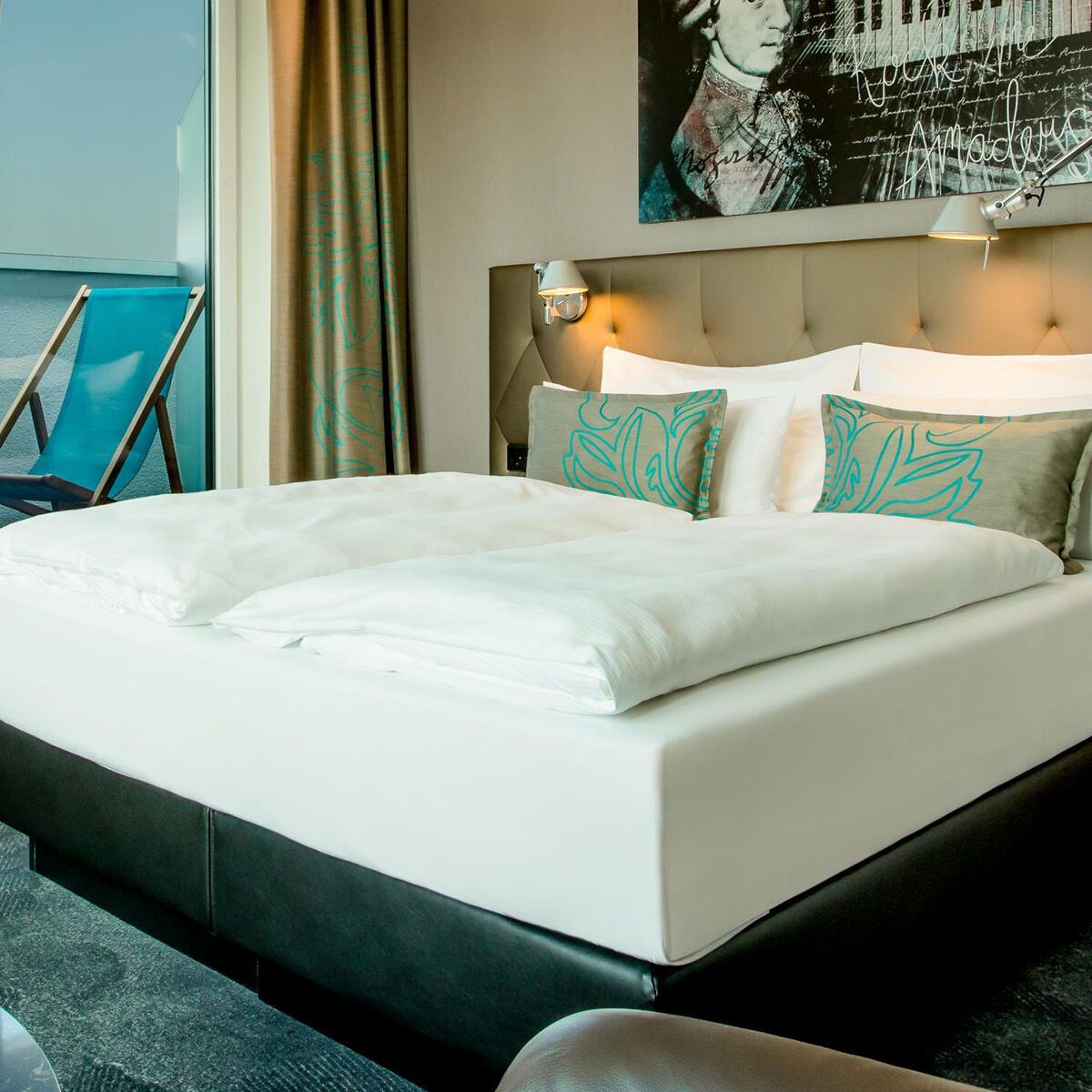 Modernes Hotelzimmer mit großem, gemütlichem Doppelbett, stilvoller Wanddekoration und Zugang zu einem Balkon mit Sitzgelegenheit. Helle, freundliche Atmosphäre mit modernen Möbeln und entspannendem Ausblick.