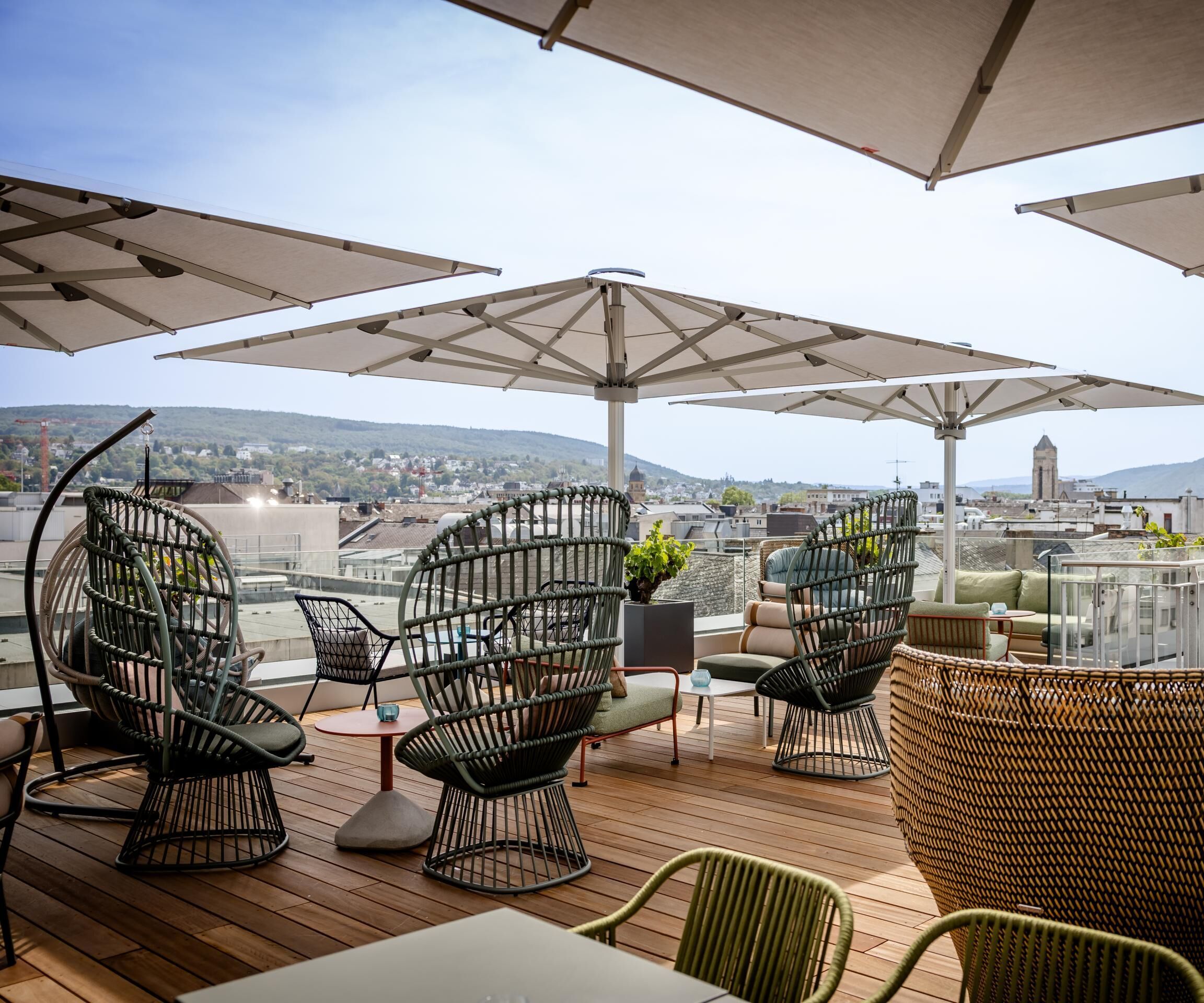 Dachterrasse mit komfortablen Sitzgelegenheiten, großen Sonnenschirmen und Blick über die Stadt bis zu den Bergen, ideal zum Entspannen und Genießen der Aussicht.
