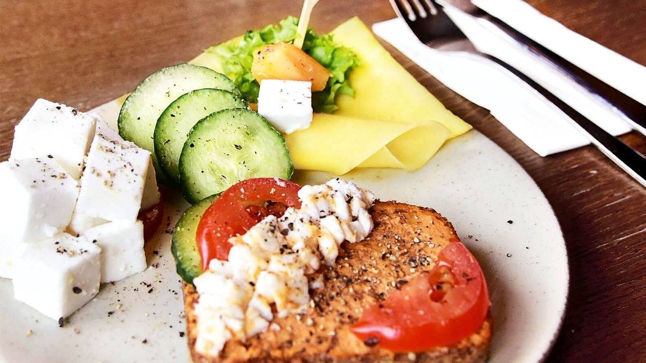 Frischer Frühstücksteller mit Feta, Gurkenscheiben, Tomaten, Salat, Käse und Vollkornbrot, appetitlich angerichtet, ideal für einen gesunden Start in den Tag.