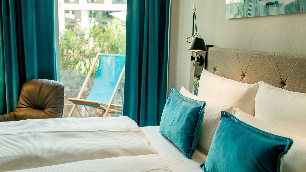 Designhotel Köln Messe Motel One Zimmer mit großem Bett sowie Balkonzugang und Liegestuhl