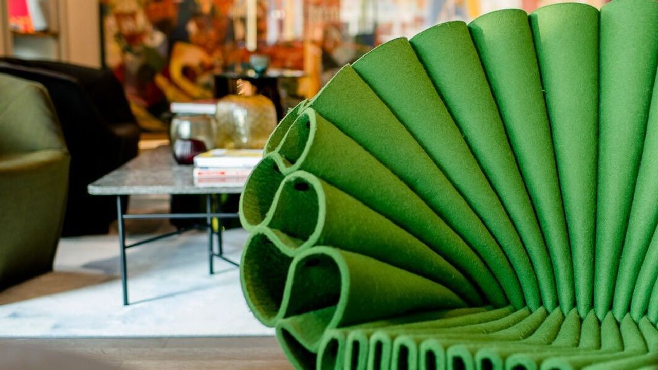 Grüner Design Sessel mit wellenförmigem Polsterdesign in einem stilvoll eingerichteten Wohnbereich mit Kunstwerken im Hintergrund.