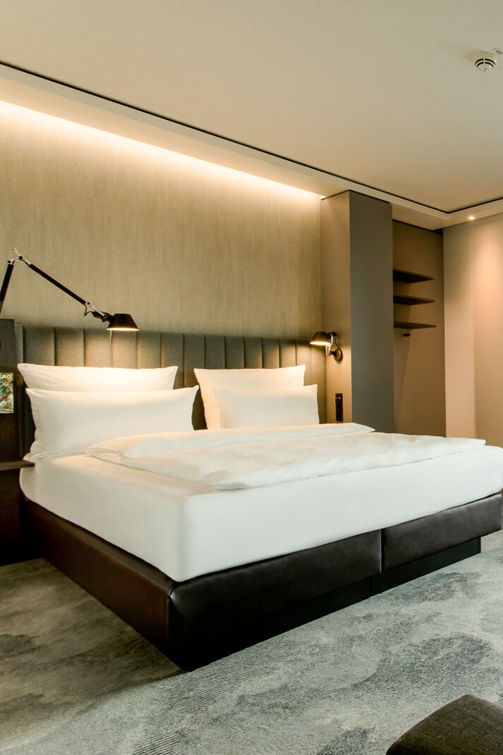 Hotelzimmer mit großem Doppelbett, indirekter Beleuchtung, grünem Vorhang und Blick auf Bäume. Design mit Sitzbereich, Schreibtisch und beruhigender Atmosphäre für erholsamen Aufenthalt.