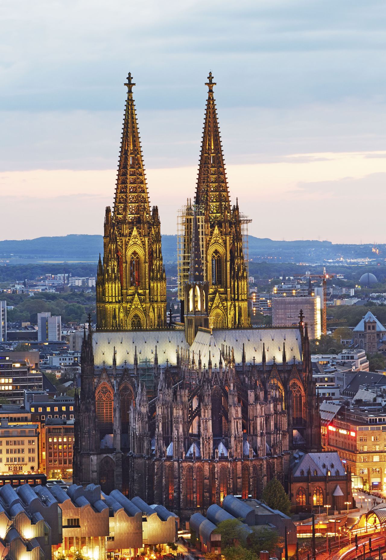 Beeindruckender Blick auf den beleuchteten Kölner Dom bei Abenddämmerung, umgeben von der modernen Stadtlandschaft Kölns.