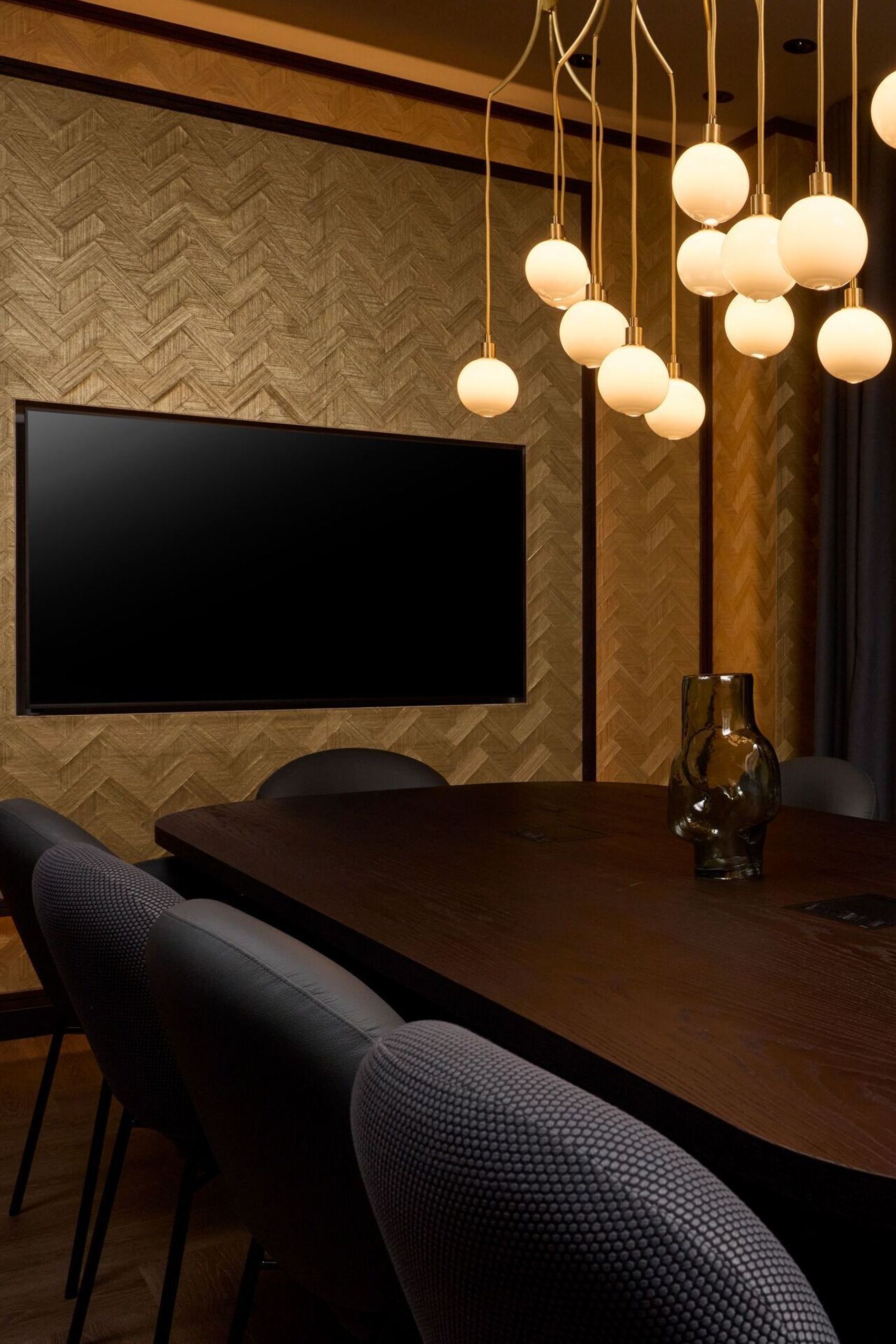 Hotel Frankfurt Metropolitan The Cloud One meeting room with dark wooden table, comfortable chairs, soft lighting from hanging ball lamps and a large flat screen on the wall, ideal for meetings and business appointments.