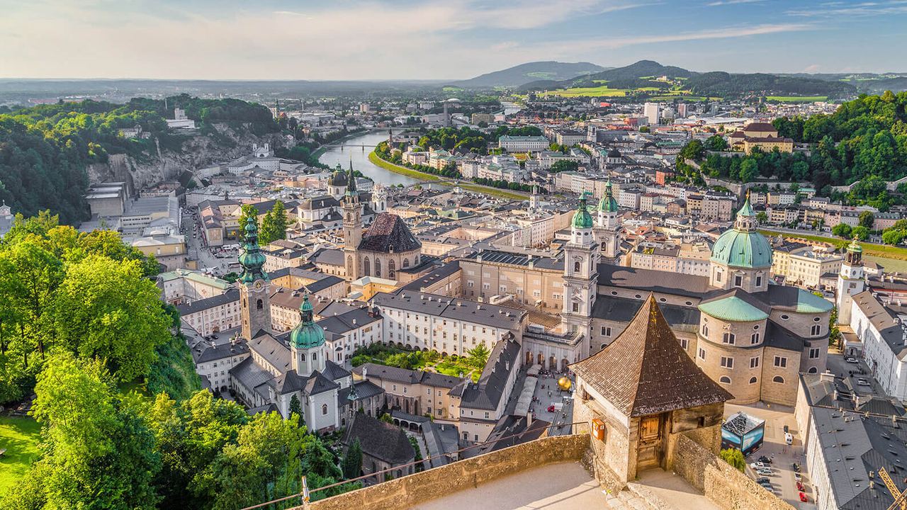 Panoramablick auf die historische Altstadt mit markanten Kuppeln und Türmen, eingebettet in grüne Hügel und den fließenden Fluss, unter einem klaren, blauen Himmel