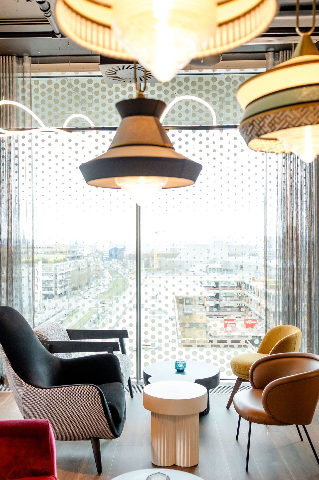 Hotel Karlsruhe Motel One Rooftop Bar mit bequemen Sesseln in warmen Farben, großen Fenstern mit Blick auf die Stadt und stilvollen Hängeleuchten für entspannte Atmosphäre.