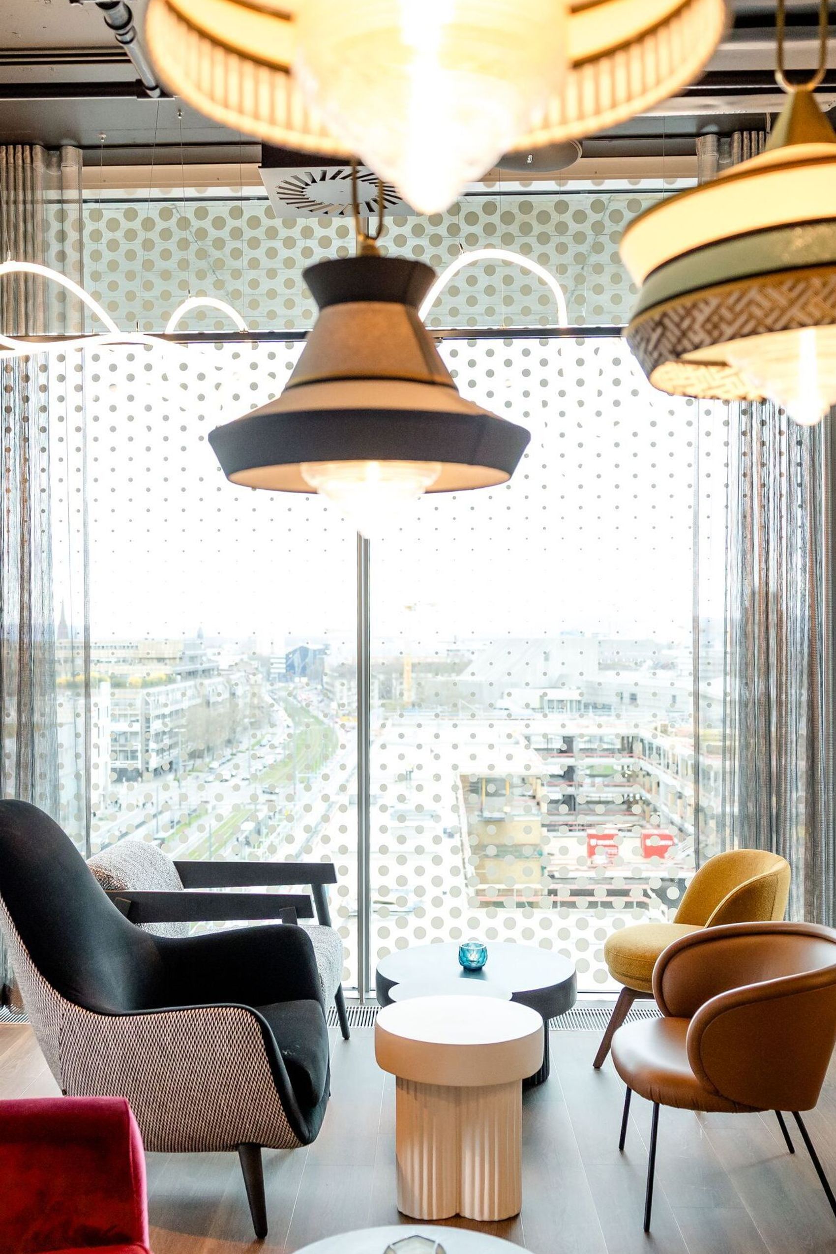 Hotel Karlsruhe Motel One Rooftop Bar mit bequemen Sesseln in warmen Farben, großen Fenstern mit Blick auf die Stadt und stilvollen Hängeleuchten für entspannte Atmosphäre.