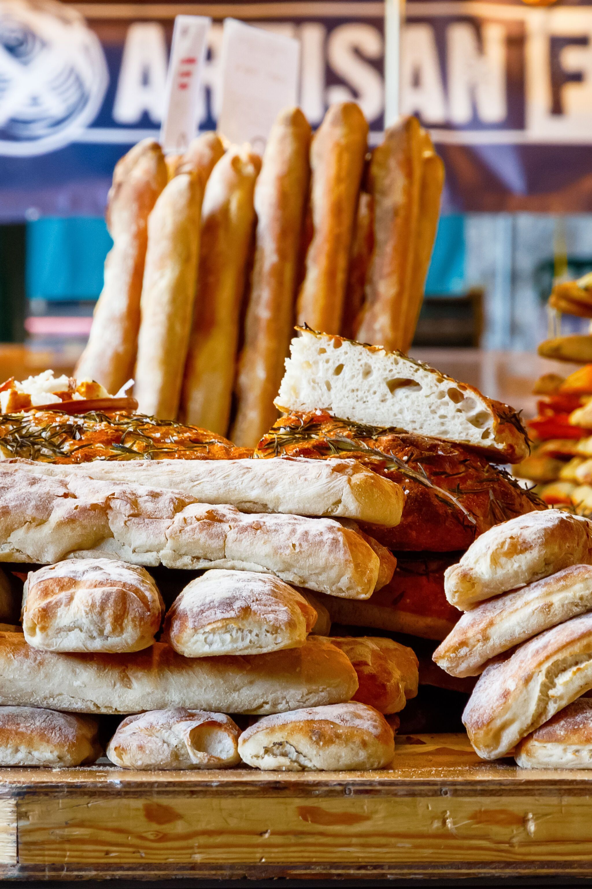 Verschiedene frische, gebackene Brotsorten und Baguettes auf einem Marktstand, beleuchtet von warmen Lichtern, vermitteln eine einladende und rustikale Atmosphäre.