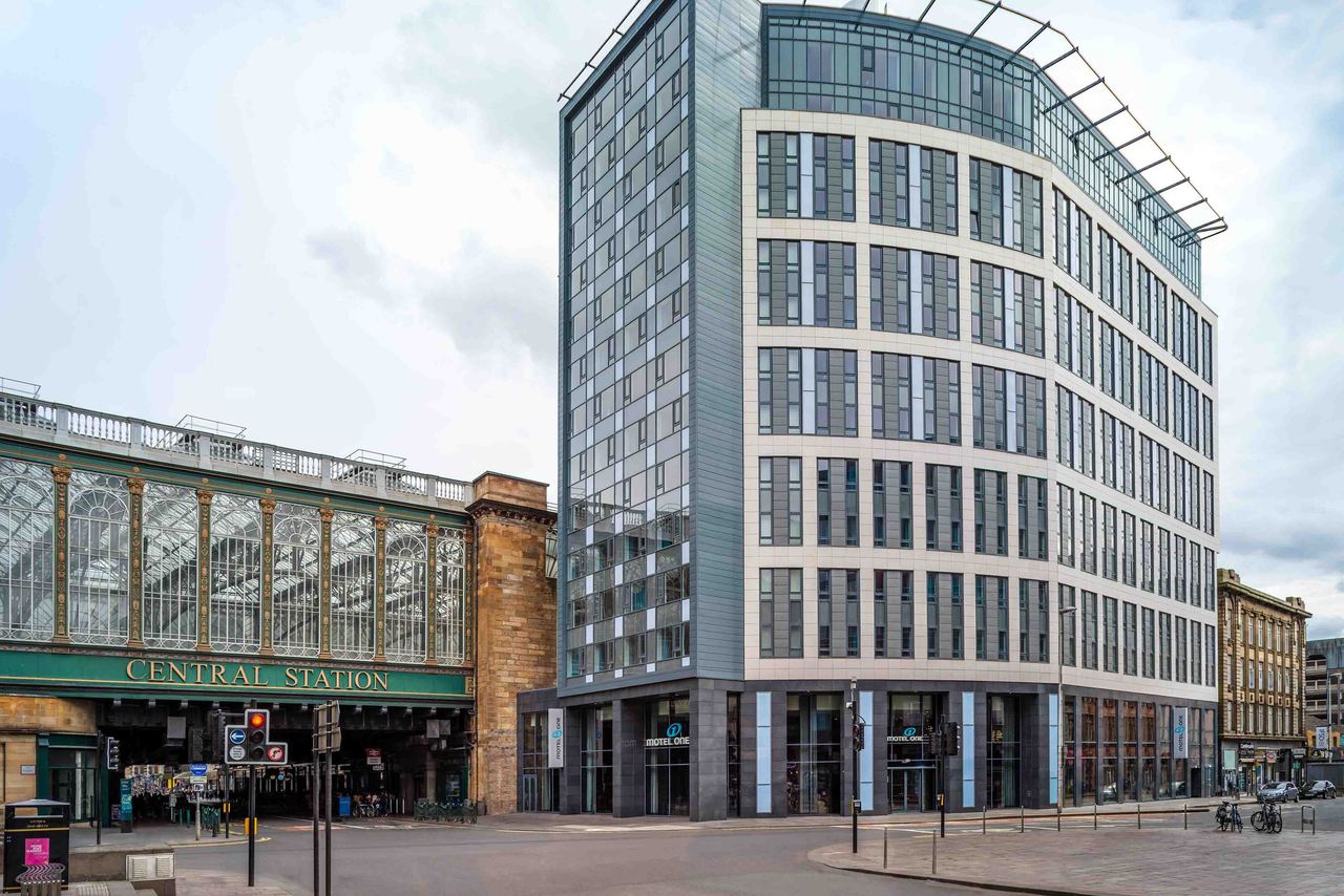 Mehrstöckiges Motel One Hotelgebäude neben dem historischen Hauptbahnhof mit großflächigen Fenstern und klarer, urbaner Architektur im städtischen Umfeld.