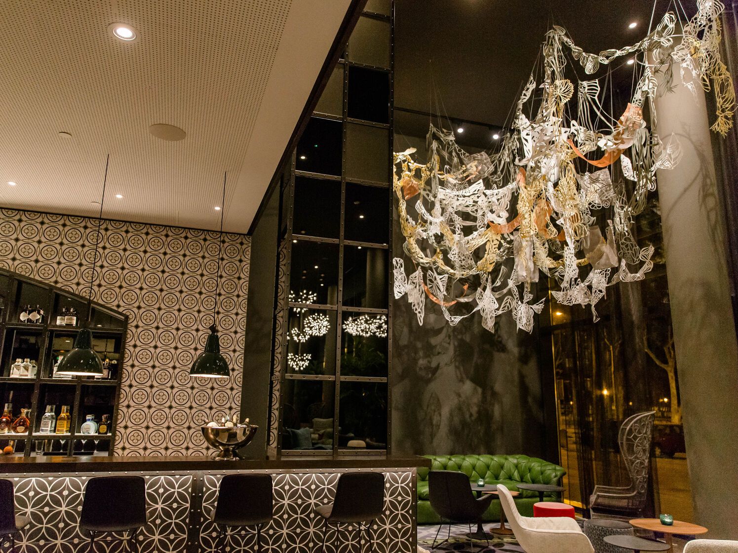 Stylisch eingerichteter Hotel-Lounge-Bereich mit gemütlichen Sitzmöbeln, dekorativem Wandmuster und auffälliger, kunstvoller Deckenbeleuchtung