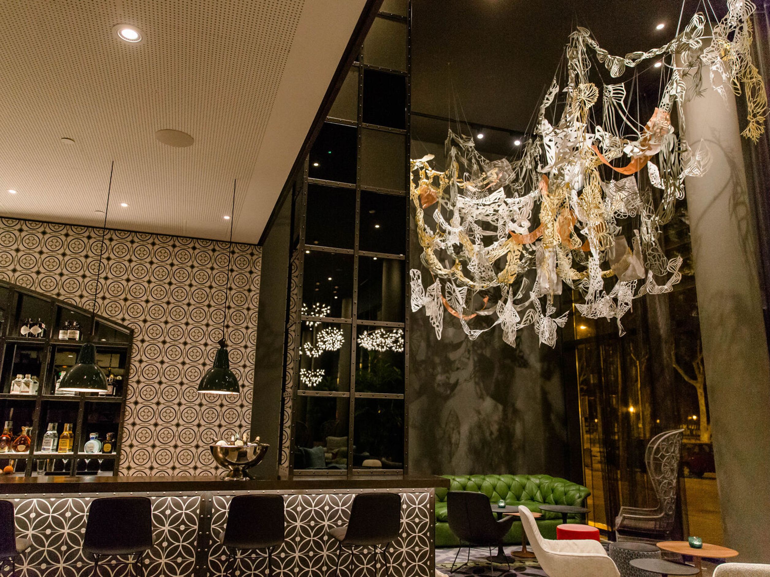 Stylisch eingerichteter Hotel-Lounge-Bereich mit gemütlichen Sitzmöbeln, dekorativem Wandmuster und auffälliger, kunstvoller Deckenbeleuchtung