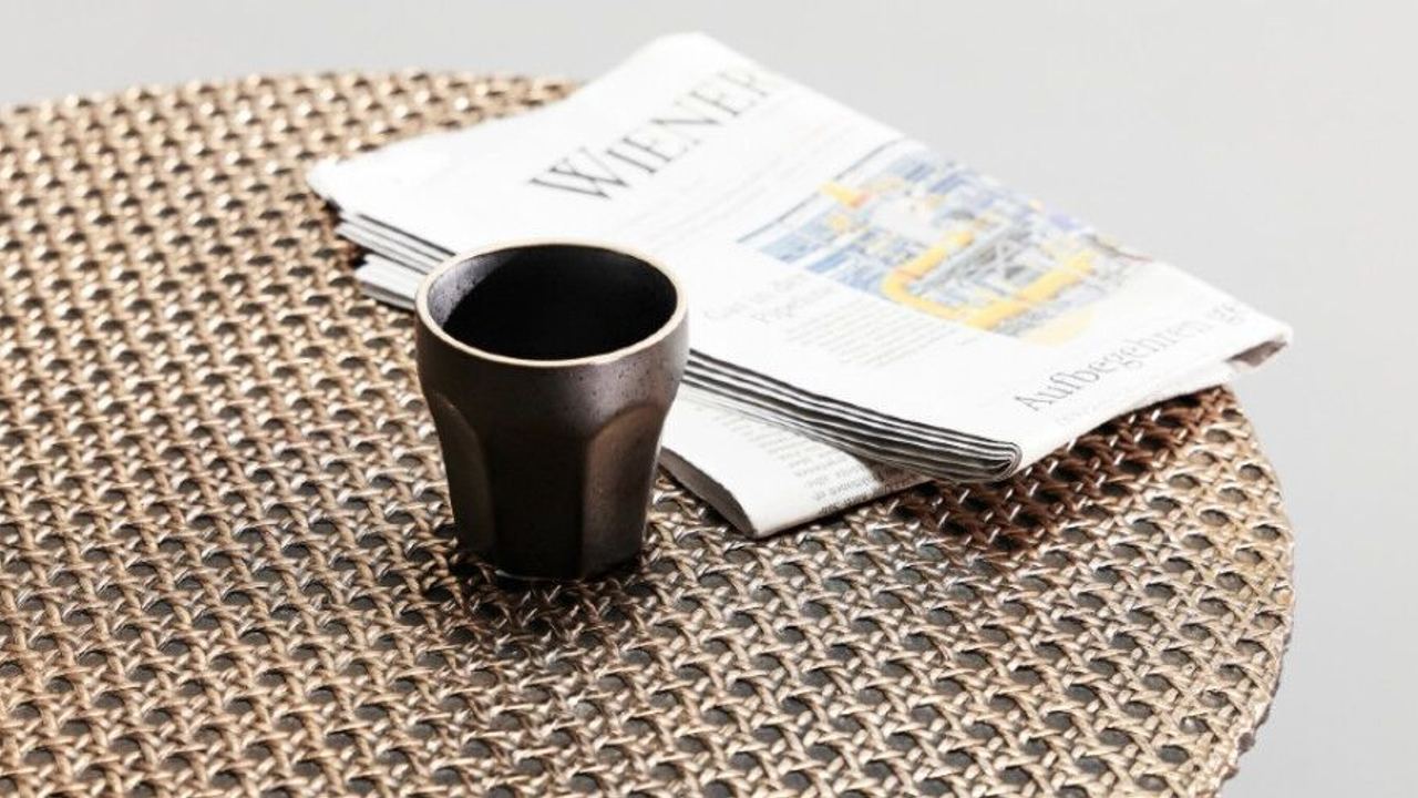 Kaffeetasse und gefaltete Zeitung liegen auf einem runden Tisch mit dekorativer Oberfläche, vermittelt entspannte Morgenstimmung.