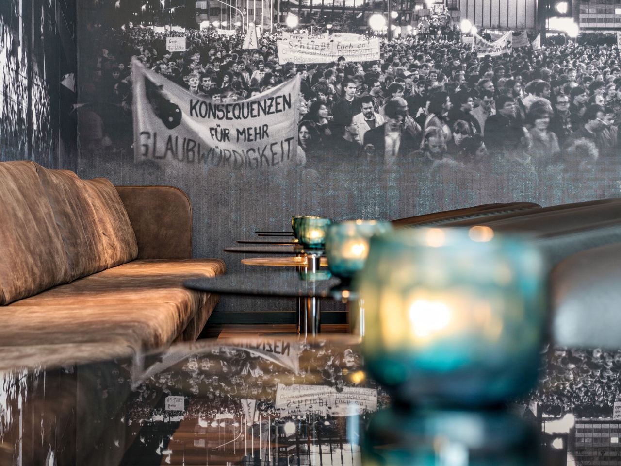 Gemütliche Lounge mit braunen Sesseln und Tischen, davor eine große Fototapete mit historischem Schwarz-Weiß-Bild einer Demonstration für mehr Glaubwürdigkeit.