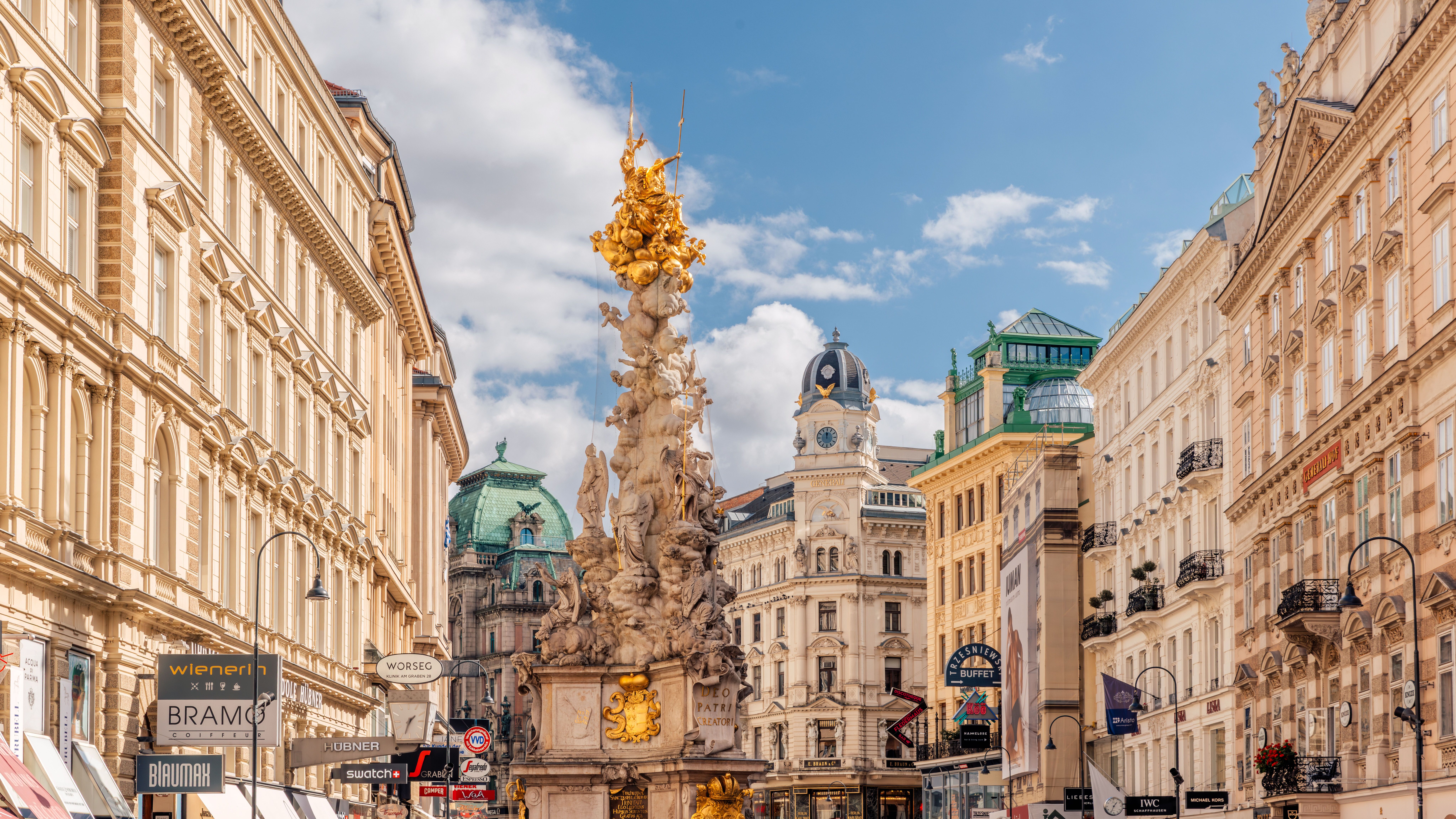 Historische Wiener Innenstadt mit prächtigen barocken Gebäuden, zentraler kunstvoll verzierter Säule und lebhaftem Straßenbild unter blauem Himmel.