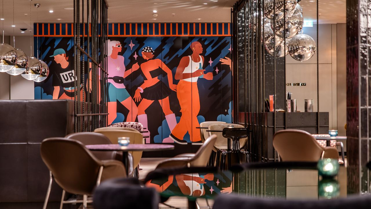 Hotel Berlin-Potsdamer Platz Motel One Moderne Hotelbar mit stilvoller Beleuchtung, gemütlichen Sitzgelegenheiten und farbenfrohem Wandbild mit dynamischen Figuren, die Bewegung und Lebendigkeit ausdrücken.