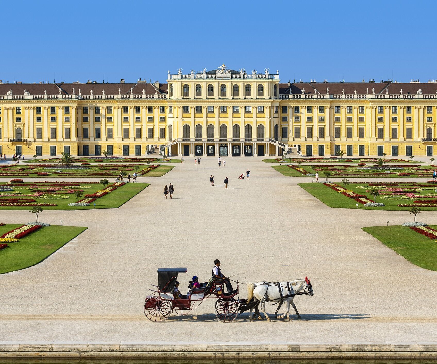 Weitläufiges Barockschloss mit symmetrischem Garten und klaren Wegen, davor eine Pferdekutsche, die eine ruhige, historische Atmosphäre vermittelt.