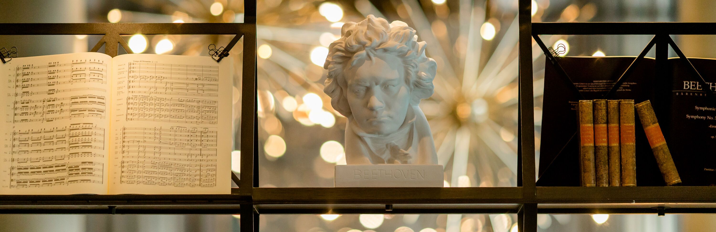 Büste von Beethoven im Motel One zwischen offener Notenpartitur und klassischen Büchern, umgeben von warmem Licht.