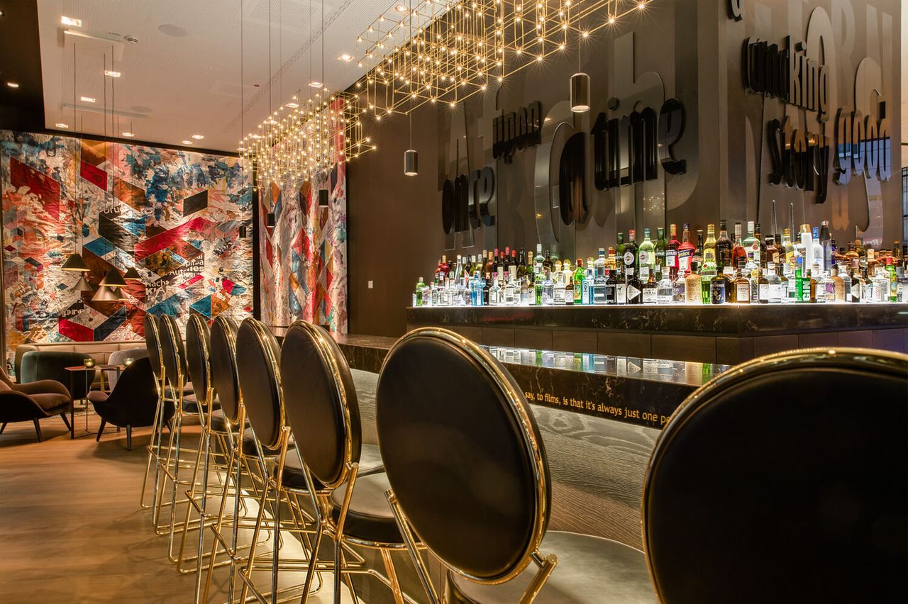 Designhotel Frankfurt Römer Motel One Bar mit Spirituosen, Barhockern und farbenfrohem Gemälde an der Wand