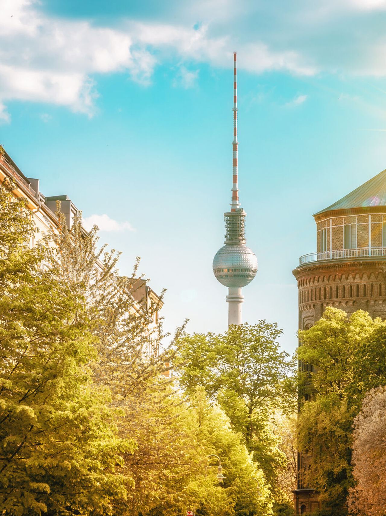 Sonnenbeschienene Straßenansicht in Berlin mit grünen Bäumen, historischen Gebäuden und dem Fernsehturm im Hintergrund, die eine einladende urbane Atmosphäre vermittelt. Sonnenbeschienene Straßenansicht in Berlin mit grünen Bäumen, historischen Gebäuden und dem Fernsehturm im Hintergrund, die eine einladende urbane Atmosphäre vermittelt.