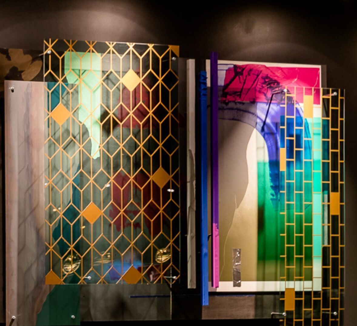 Bunte, abstrakte Kunstwerke mit geometrischen Mustern, vor dunklem Hintergrund beleuchtet, schaffen eine moderne und lebendige Atmosphäre.