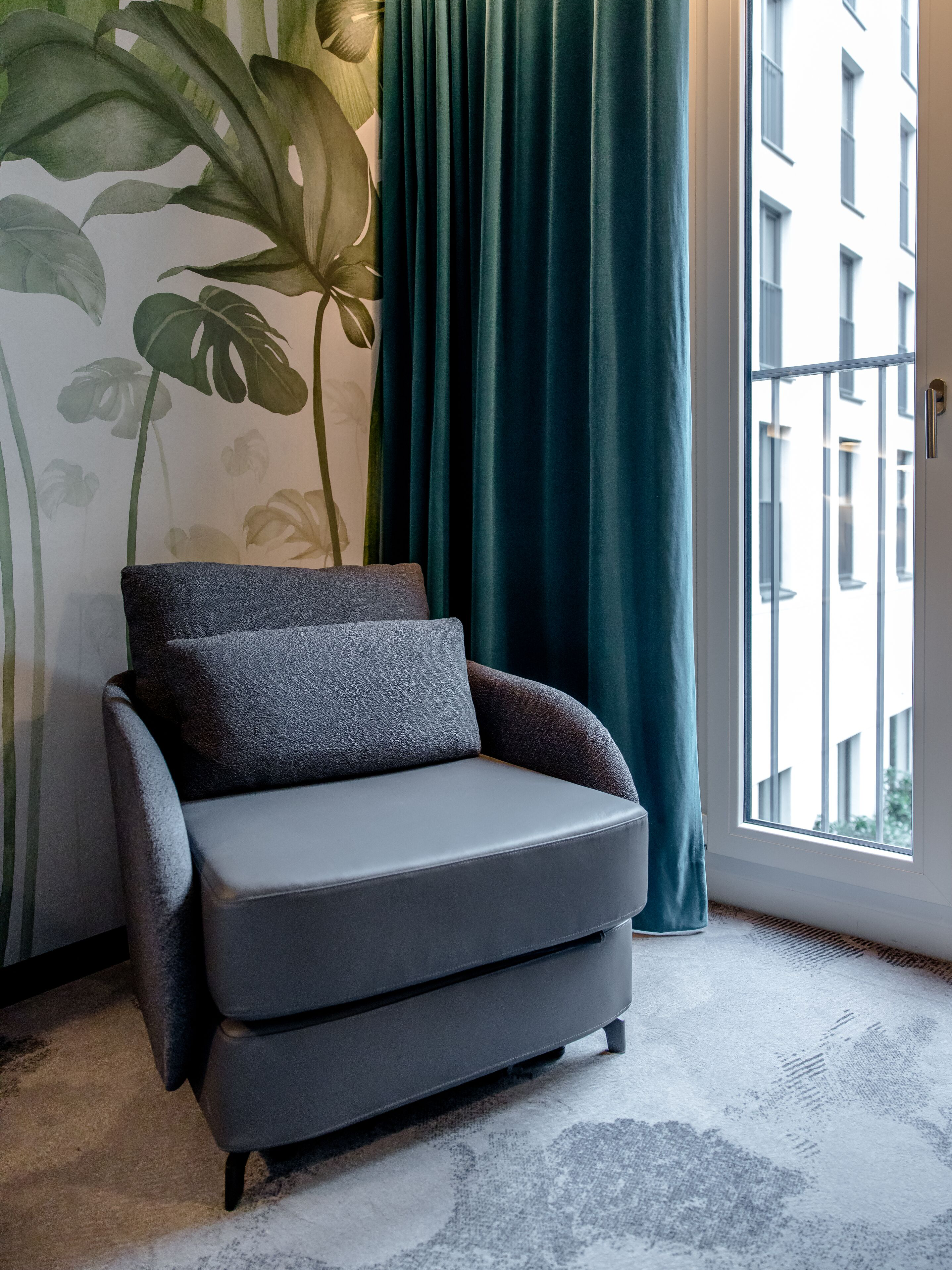 designhotel Munich Hauptbahnhof Motel One room with gray armchair in front of floor-to-ceiling window